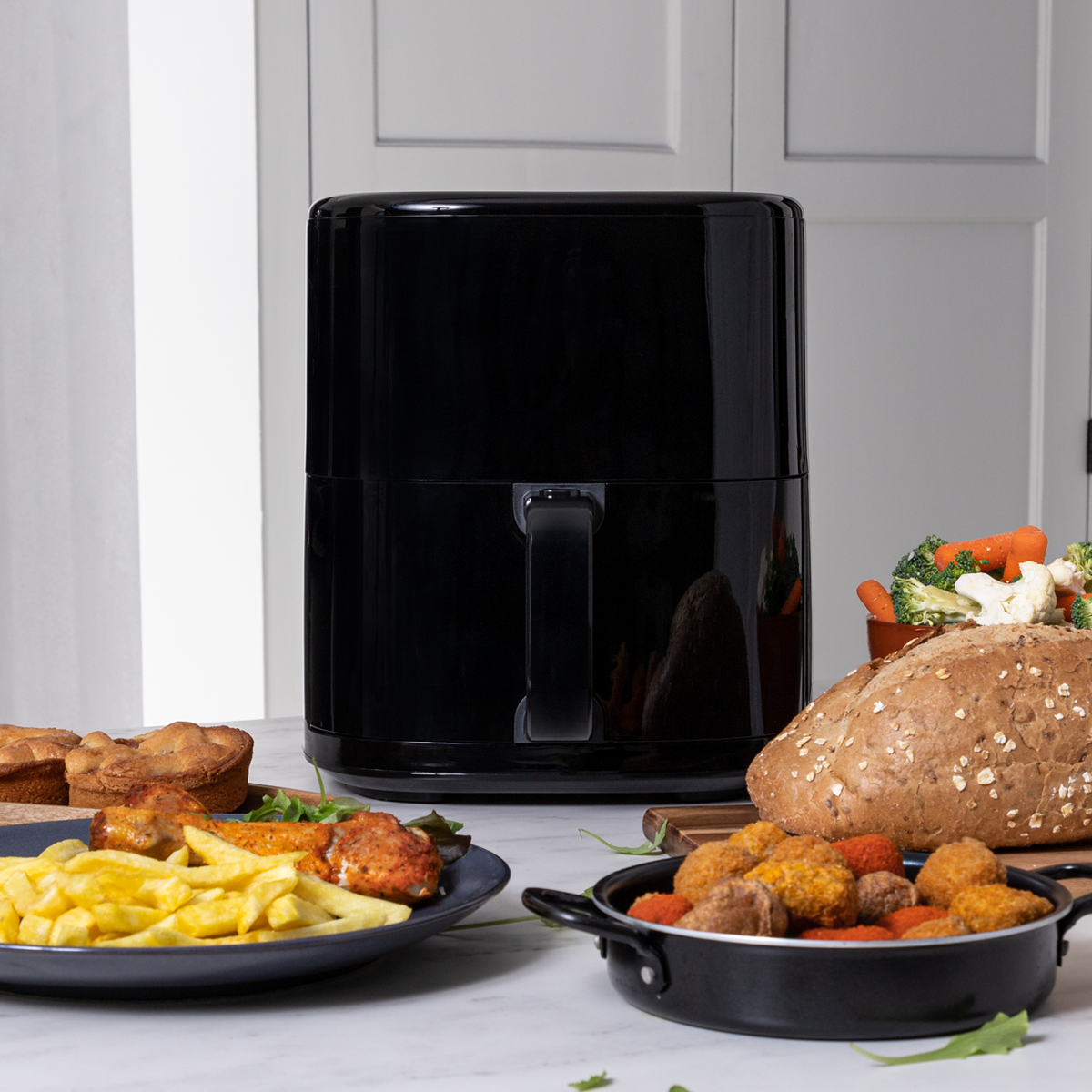 Zwarte airfryer met eten op een tafel. Inclusief friet, kip, brood en groenten.