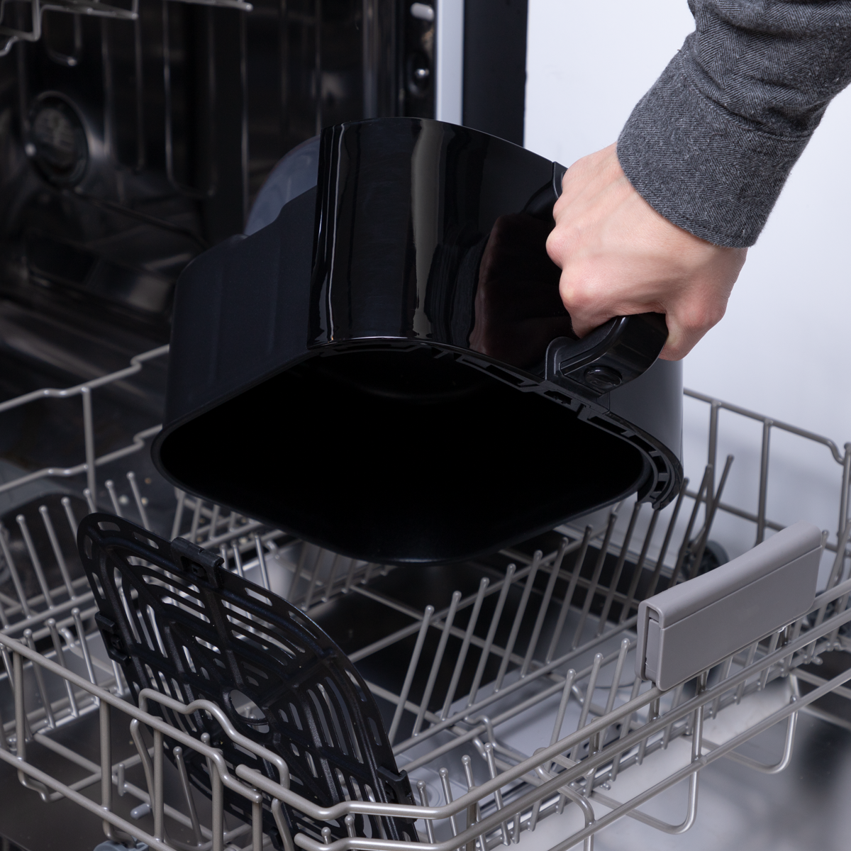 Een persoon neemt de container uit de airfryer en plaatst deze in de vaatwasser.