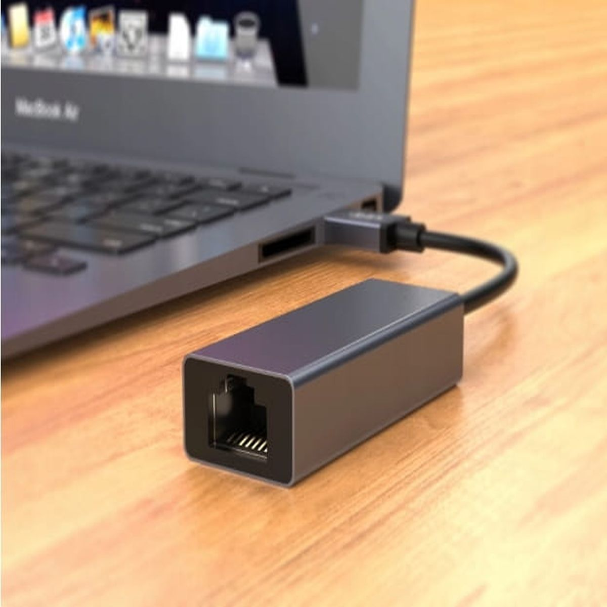 Laptop podłączony do szarego adaptera Ethernet z czarnym kablem.