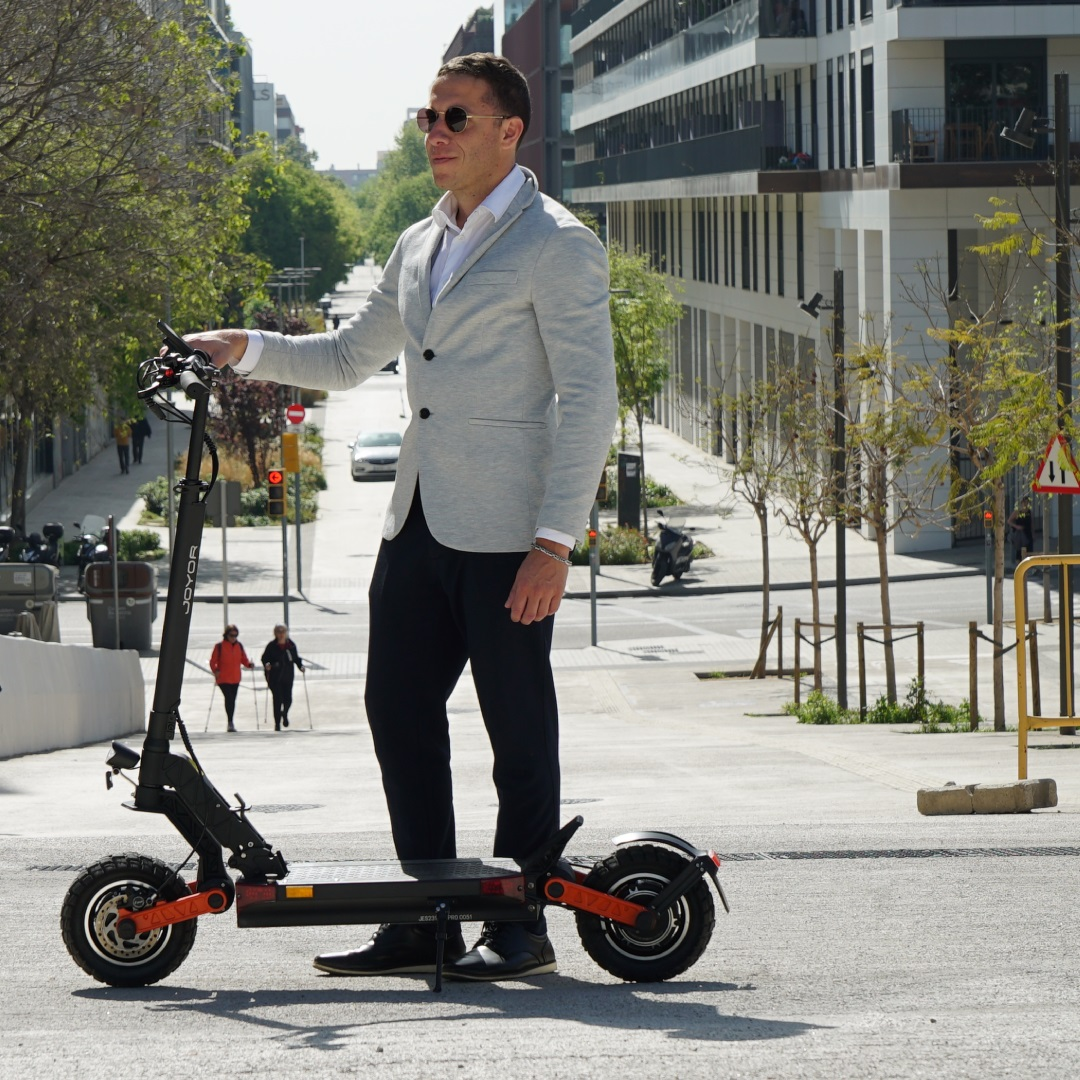 Mann mit Sonnenbrille steht neben einem Elektroroller auf einer Stadtstraße.