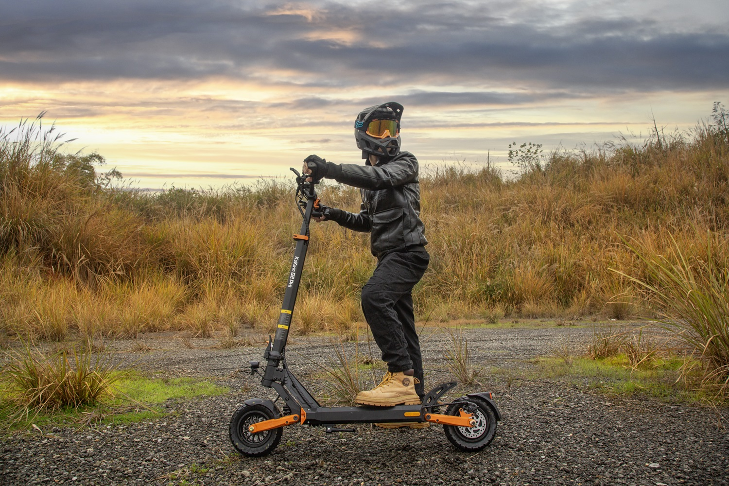 Uomo su scooter elettrico. Indossa casco, giacca e guanti. Paesaggio verde e marrone.