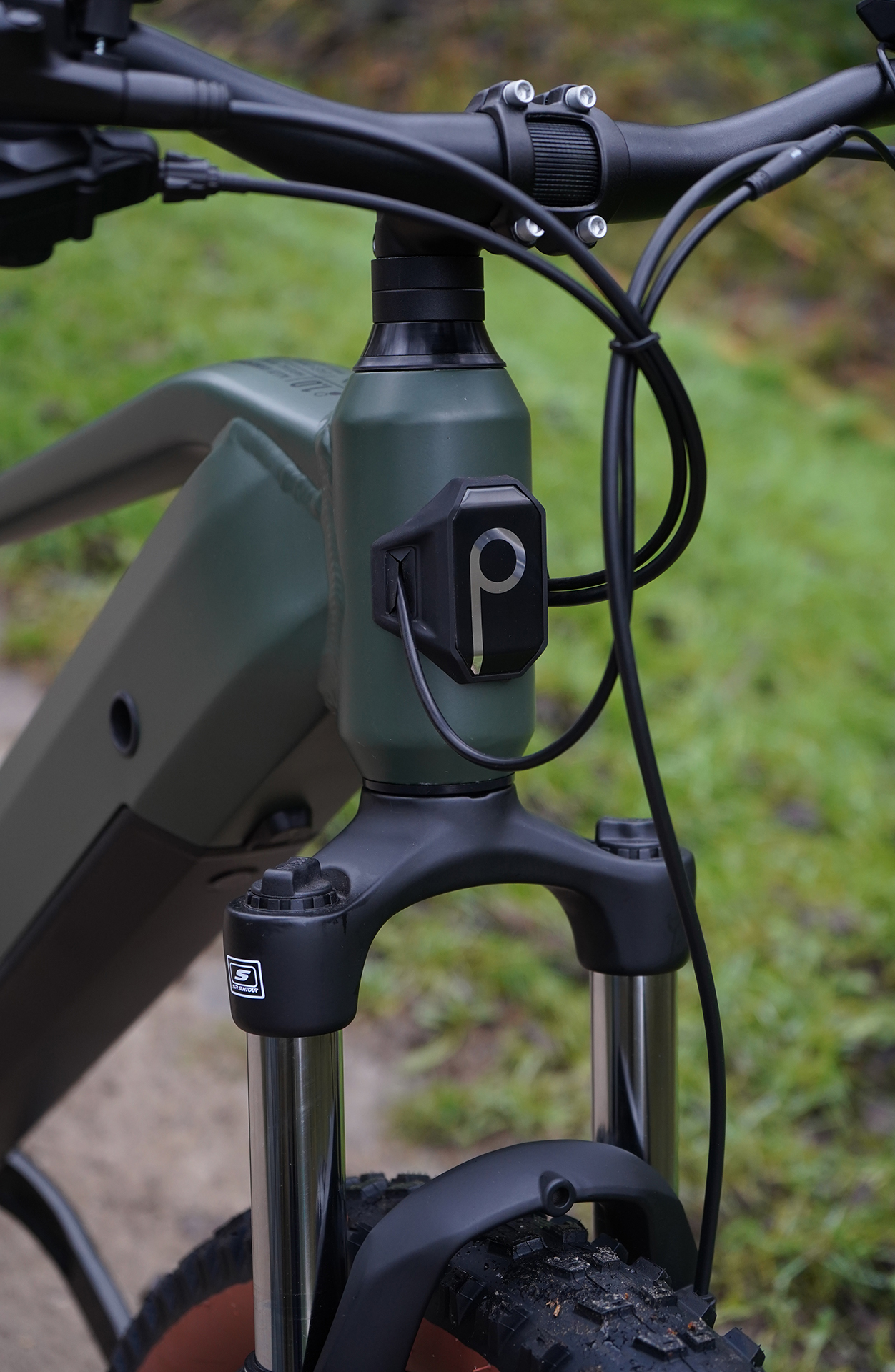 Nahaufnahme des vorderen Teils eines grün-schwarzen E-Bikes, mit unscharfem grünem Hintergrund.