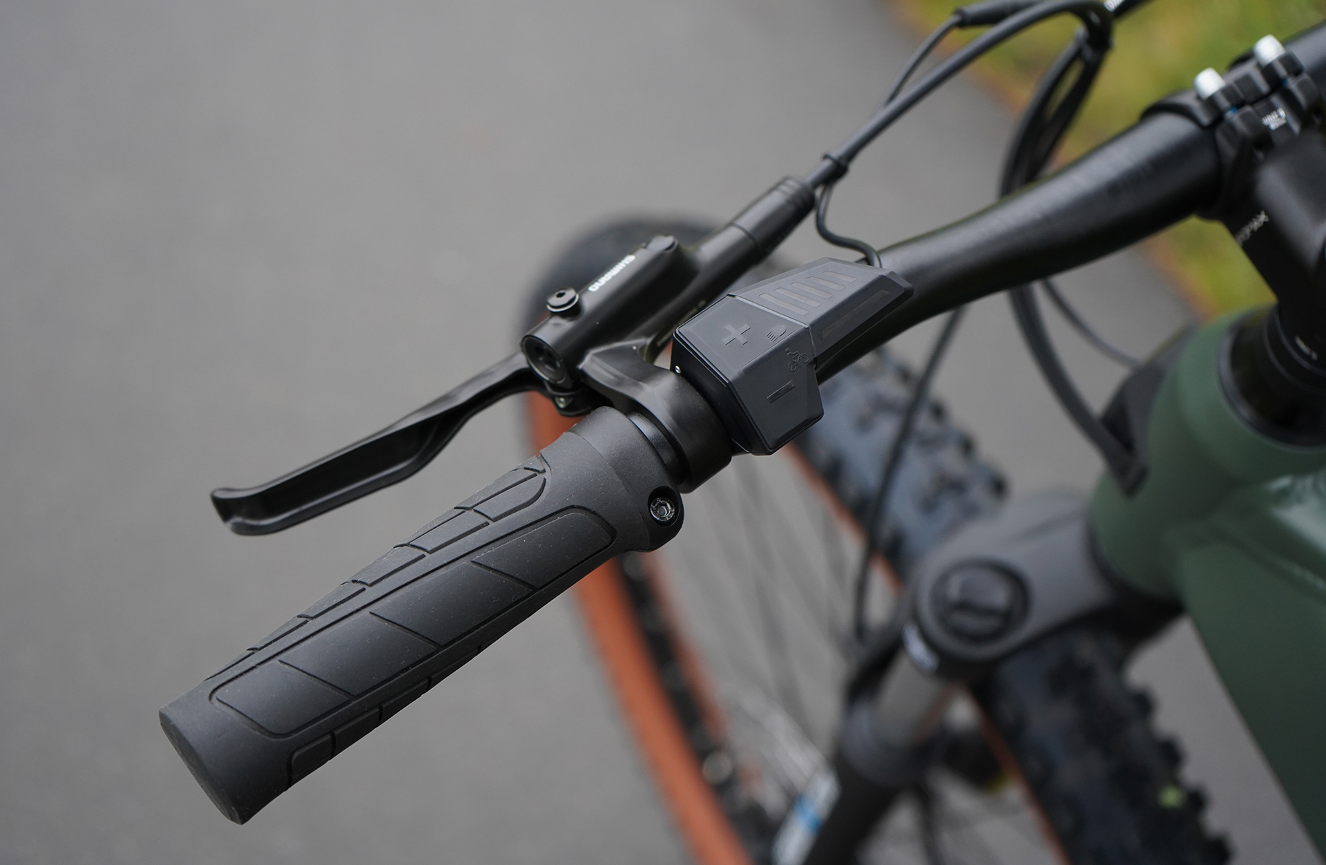 Nahaufnahme eines E-Bike-Lenkers mit Bedienelementen und Bremshebeln; der Hintergrund ist verschwommen.