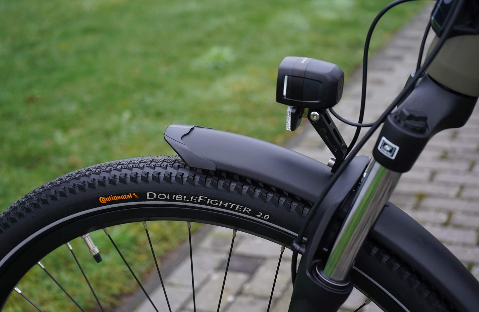 Fahrradreifen und Vorderrad mit Continental DoubleFighter 2.0. Es ist schwarz mit einem schwarzen Schutzblech und einem Scheinwerfer.