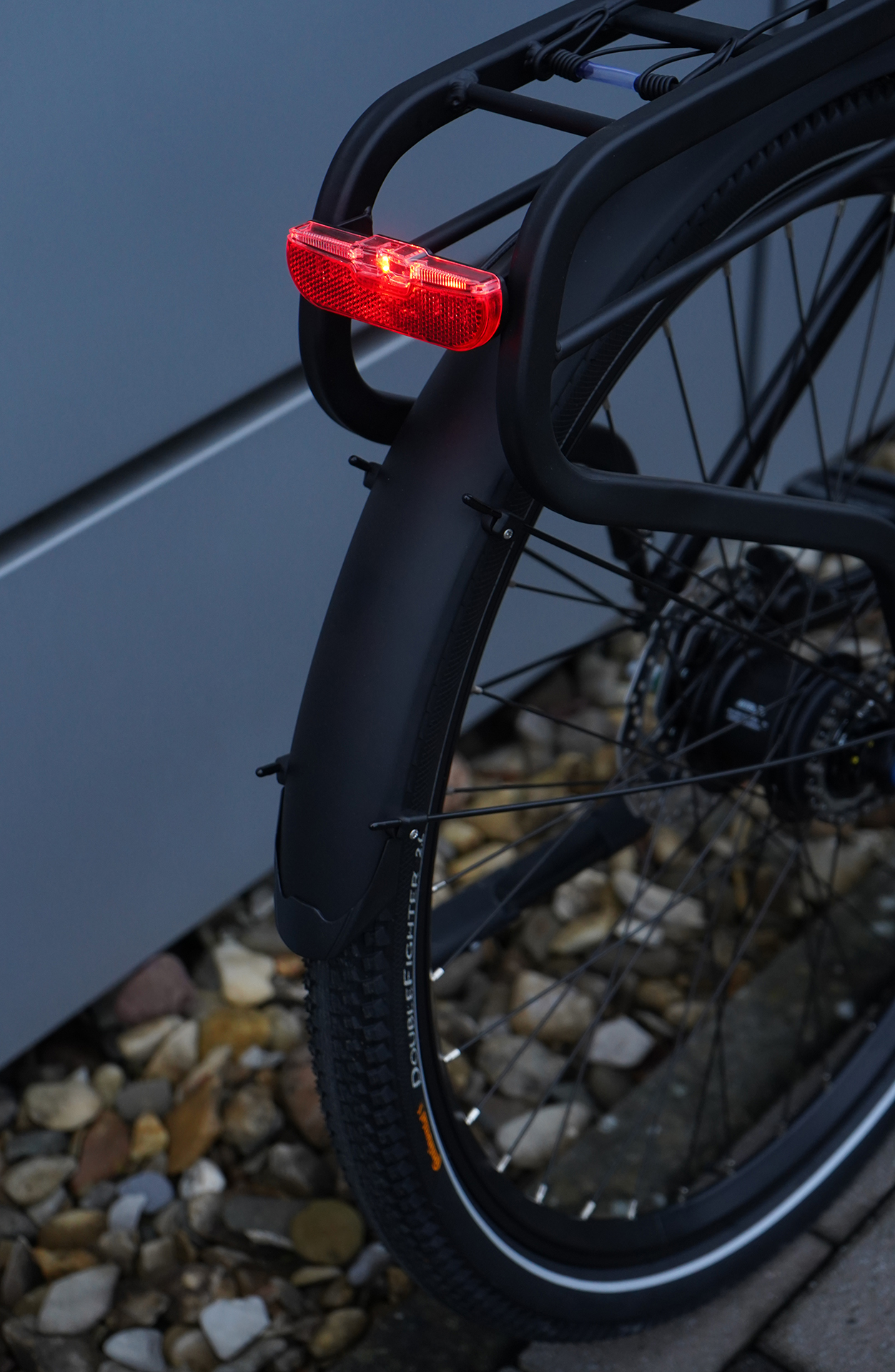 Fahrradheck mit rotem Rückstrahler, schwarzem Kotflügel und kiesigem Untergrund.