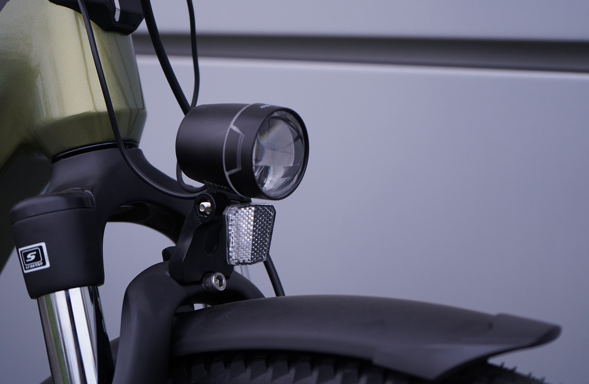 Nahaufnahme eines Fahrradscheinwerfers und Reflektors an einem Fahrrad. Der Hintergrund ist grau.