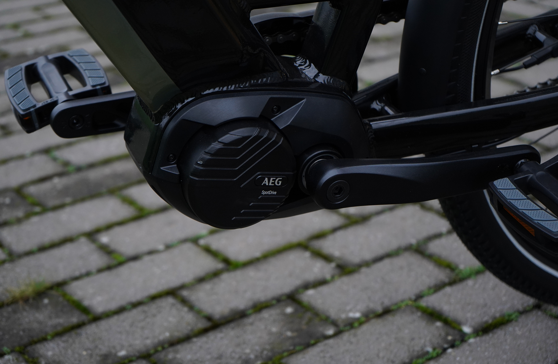 Nahaufnahme eines schwarzen Elektromotors mit AEG-Logo auf Kopfsteinpflaster.