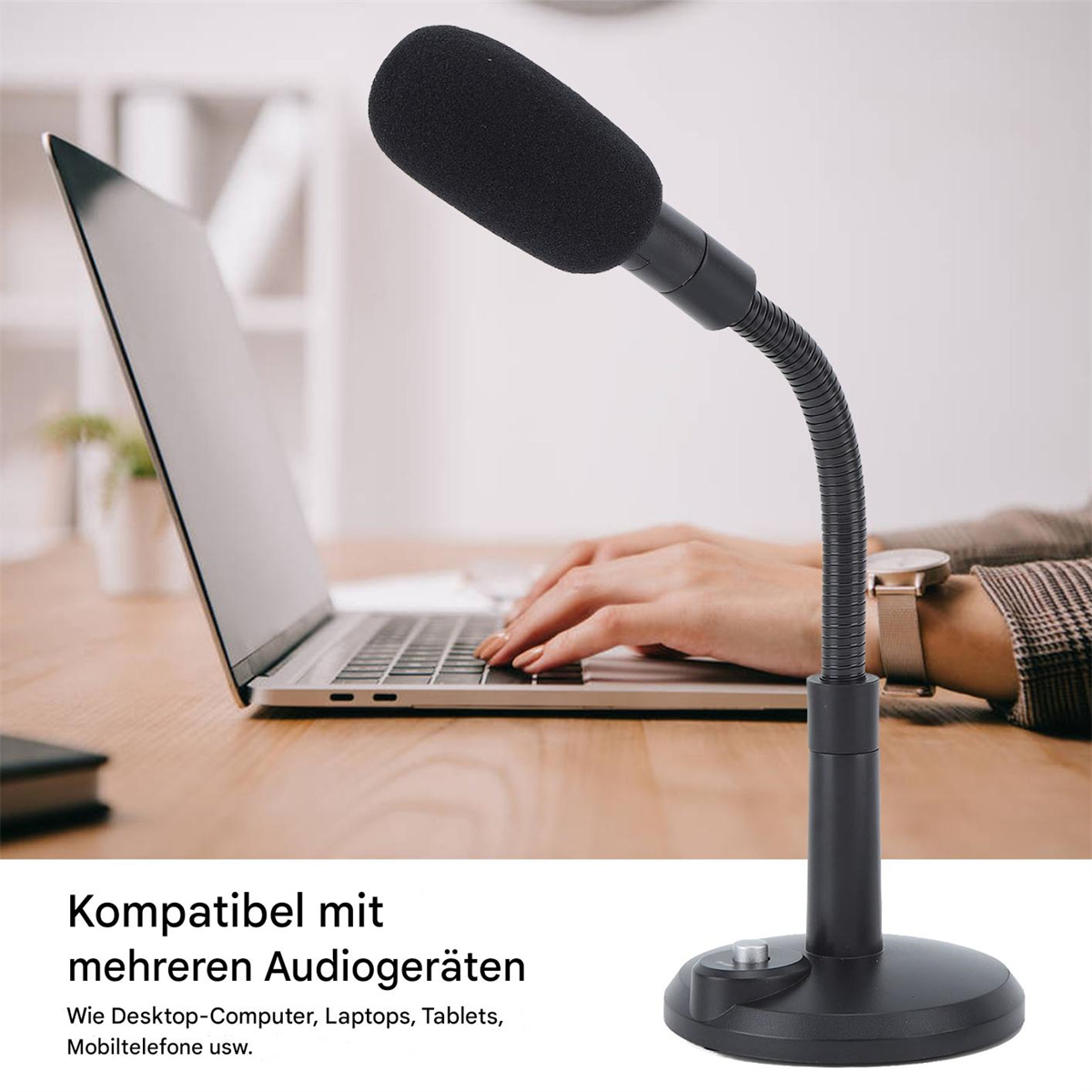 Ein schwarzes Mikrofon mit schwarzem Schaumstoffbezug steht auf einem schwarzen Ständer. Ein Laptop und Hände sind im Hintergrund.
