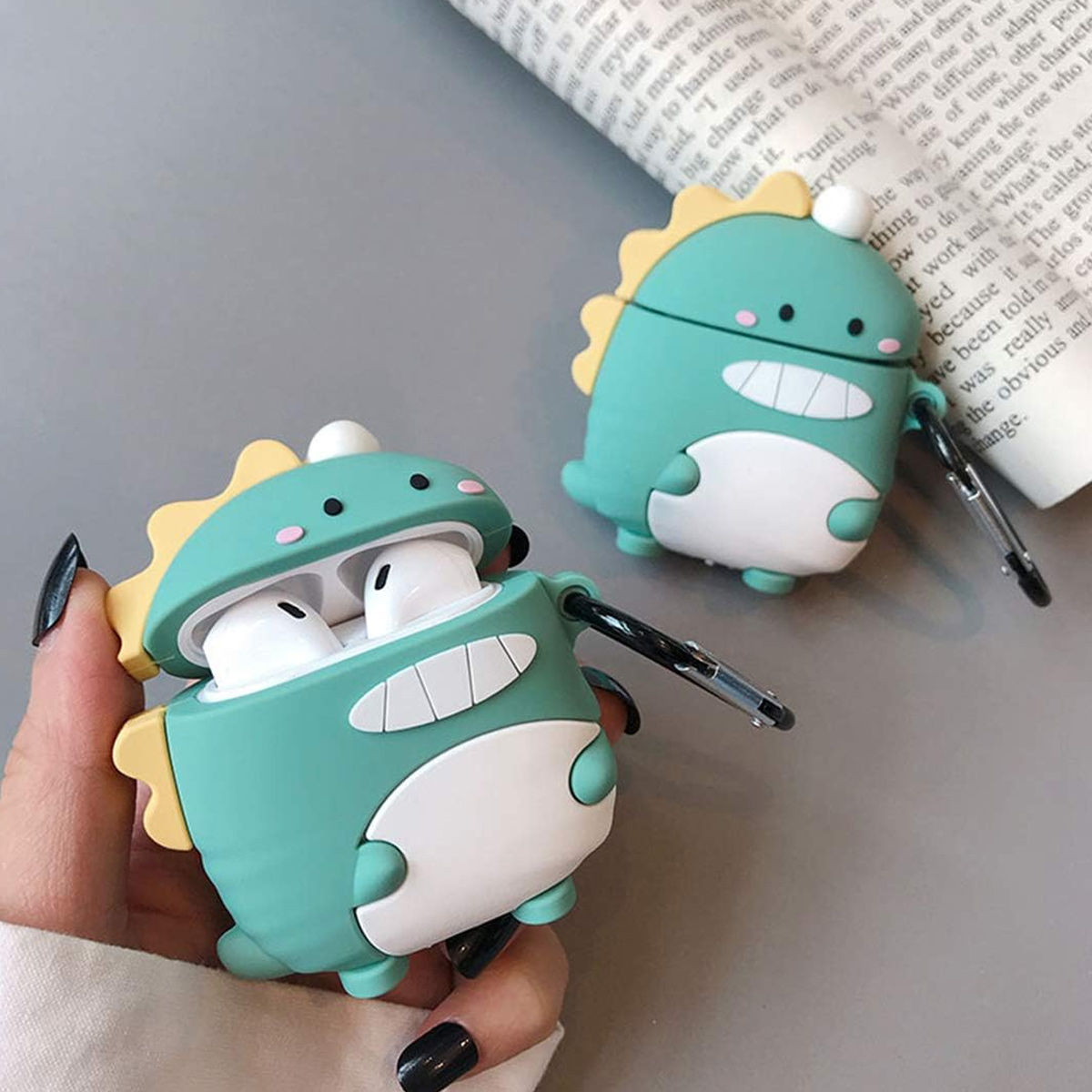 Zwei grüne AirPod-Hüllen in Dinosaurierform. Eine ist geöffnet und zeigt die AirPods. Die Hüllen haben gelbe Akzente.