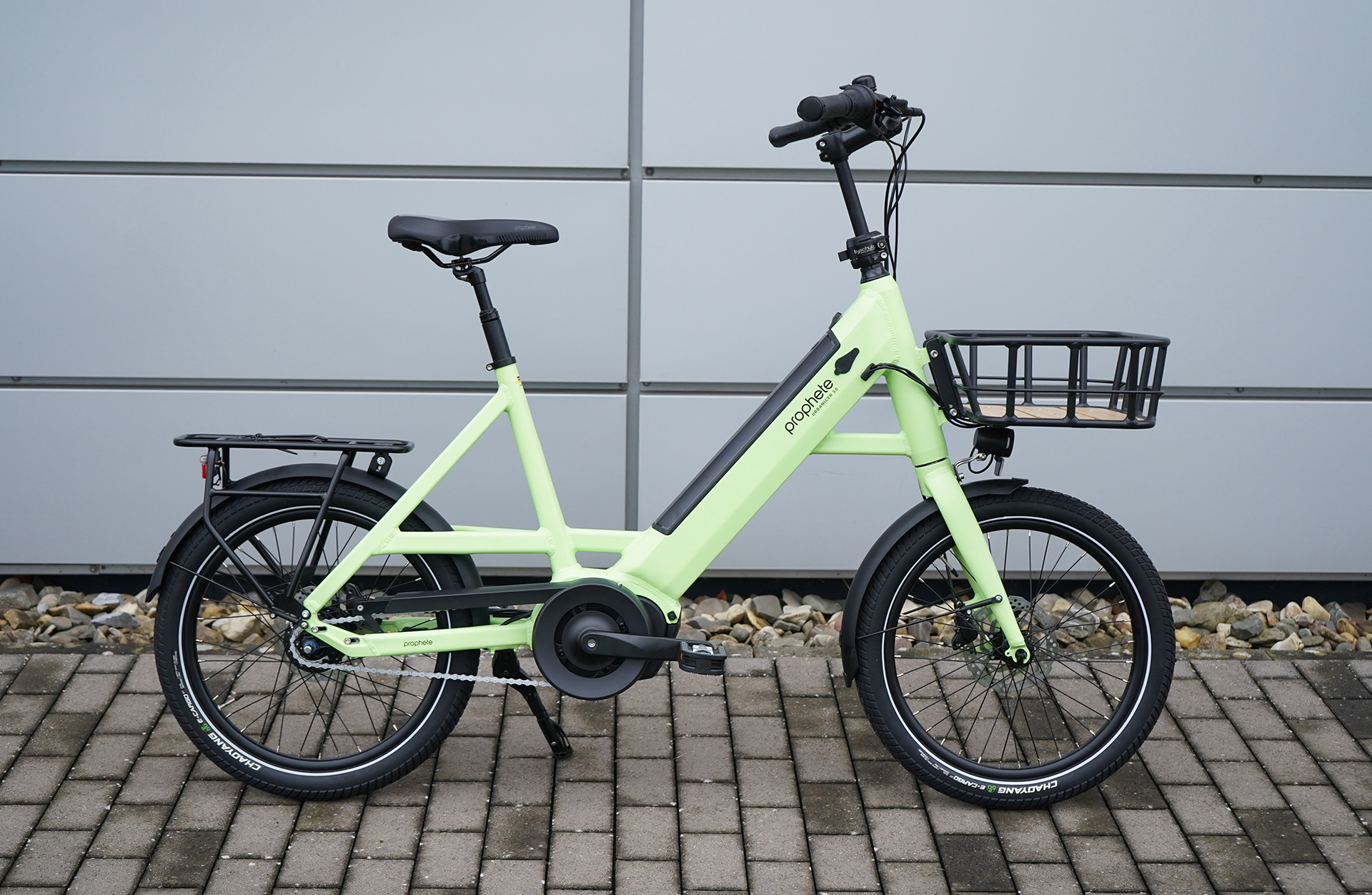 Grünes Elektrofahrrad mit Korb, geparkt auf Backsteinpflaster.