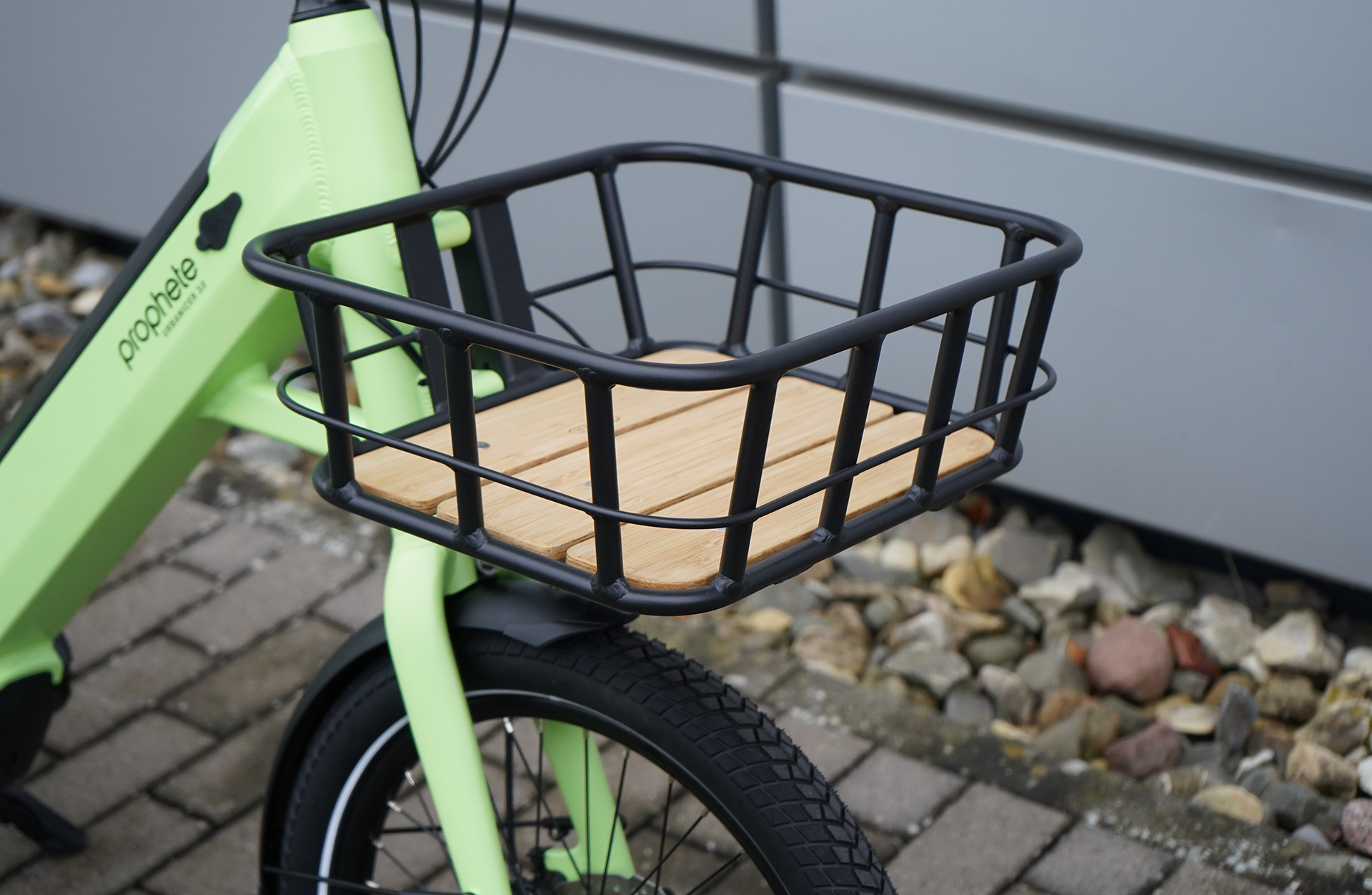Ein grünes E-Bike mit einem schwarzen quadratischen Korb mit Holzlatten, Nahaufnahme.
