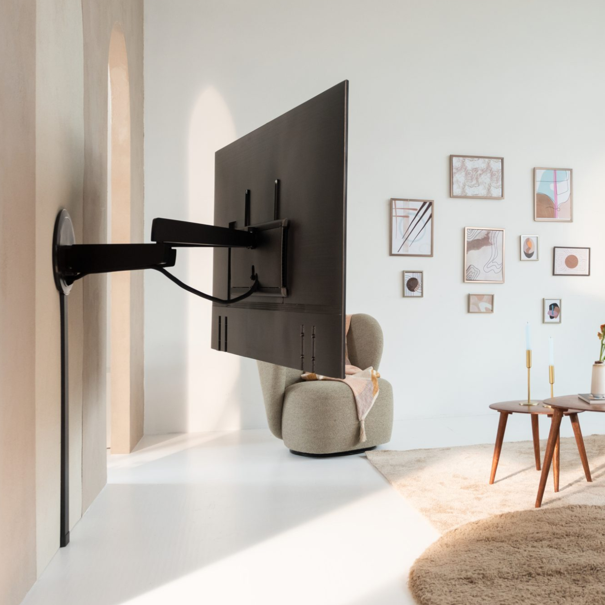 Duży telewizor zamontowany na czarnym ramieniu przymocowanym do ściany. Na ścianie obrazy i dekoracje.