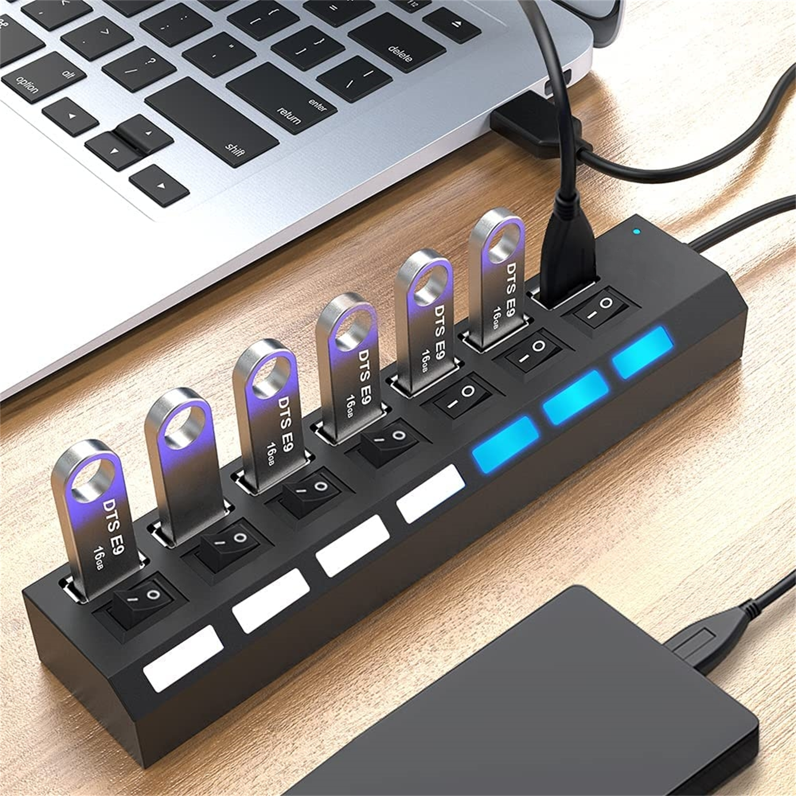 Ein Laptop, ein USB-Hub mit USB-Sticks und eine externe Festplatte liegen auf einem Holzschreibtisch.