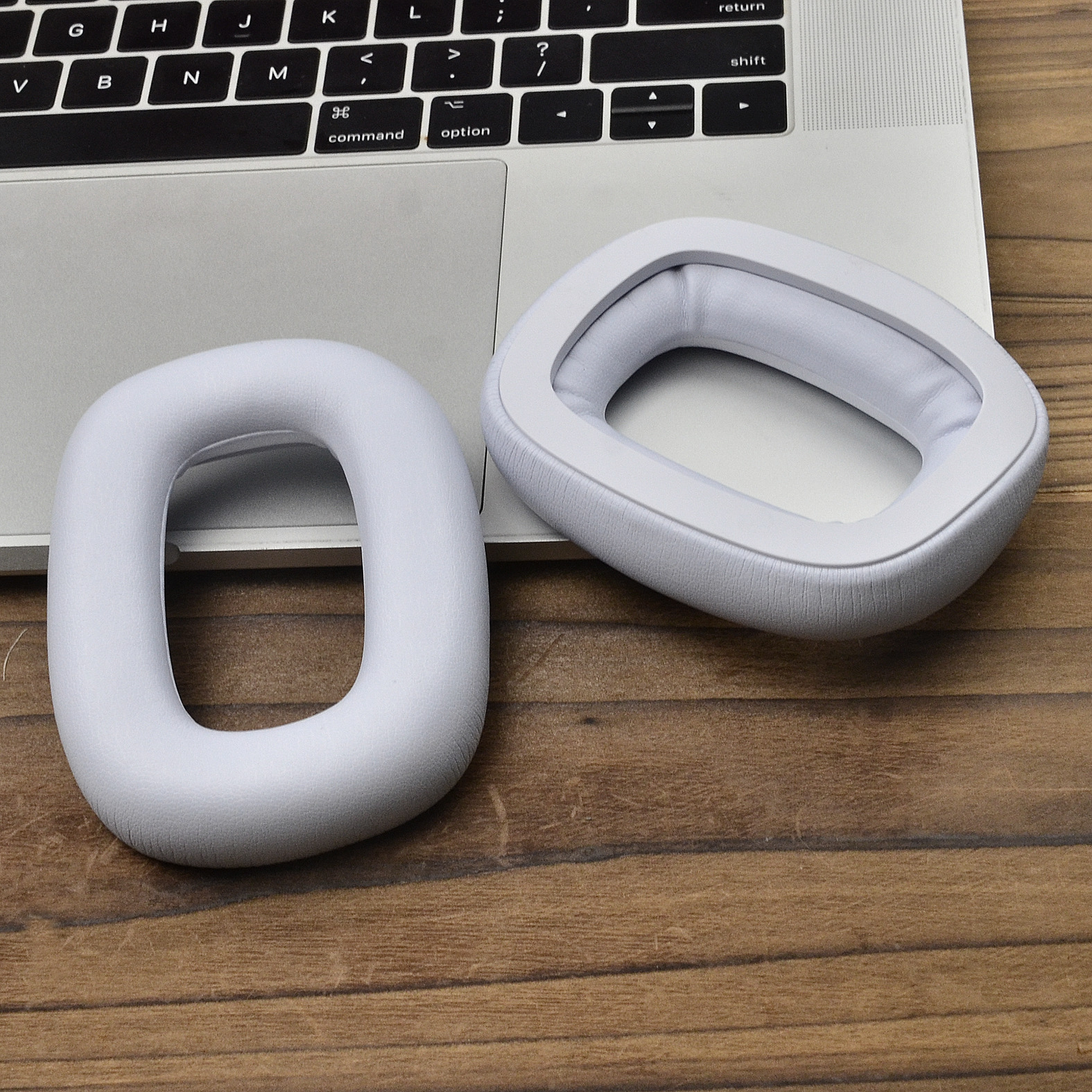 Dwie białe nauszniki na drewnianej powierzchni, obok klawiatury laptopa.