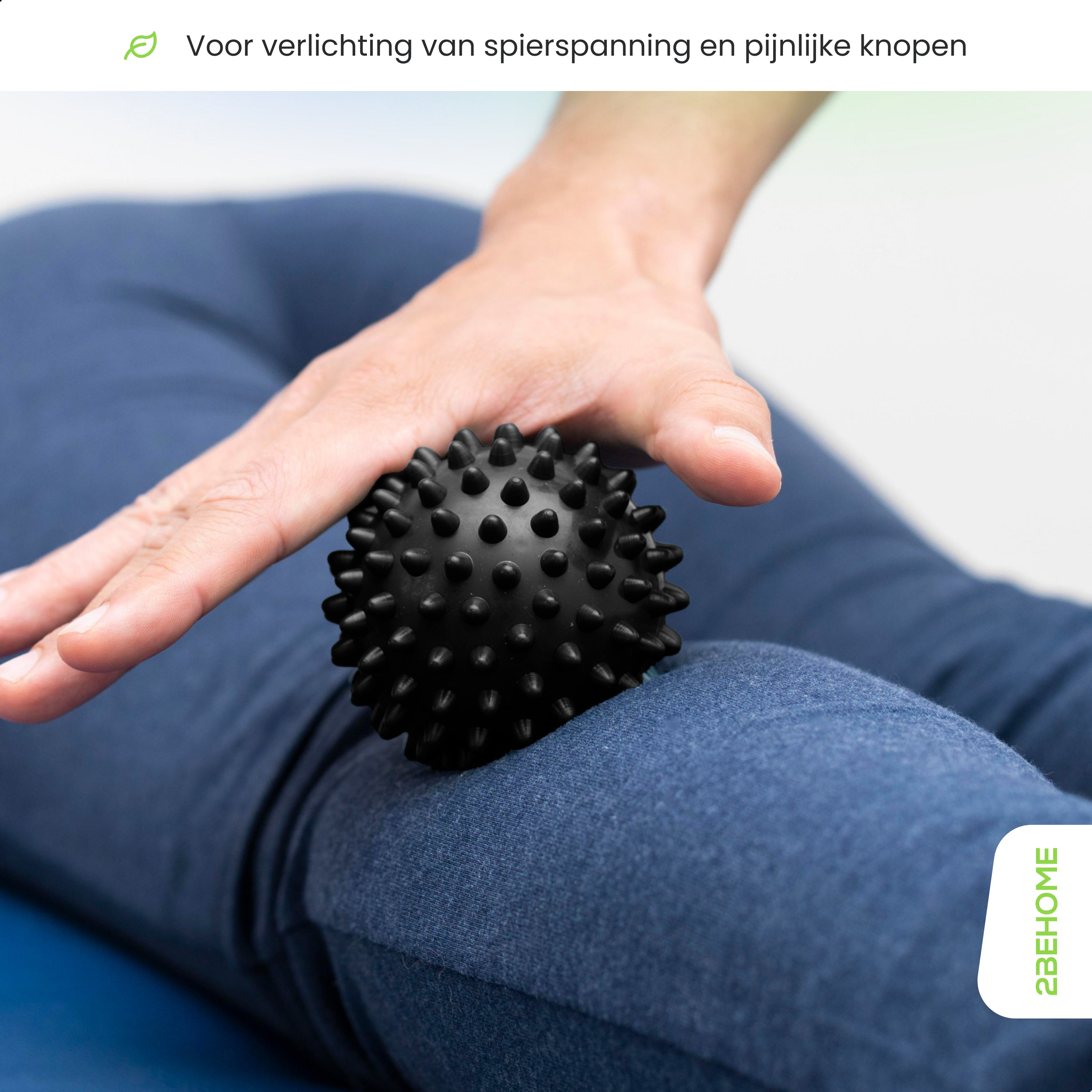 Hand presses a black spiky ball on a blue-jeaned leg. The background is out of focus.