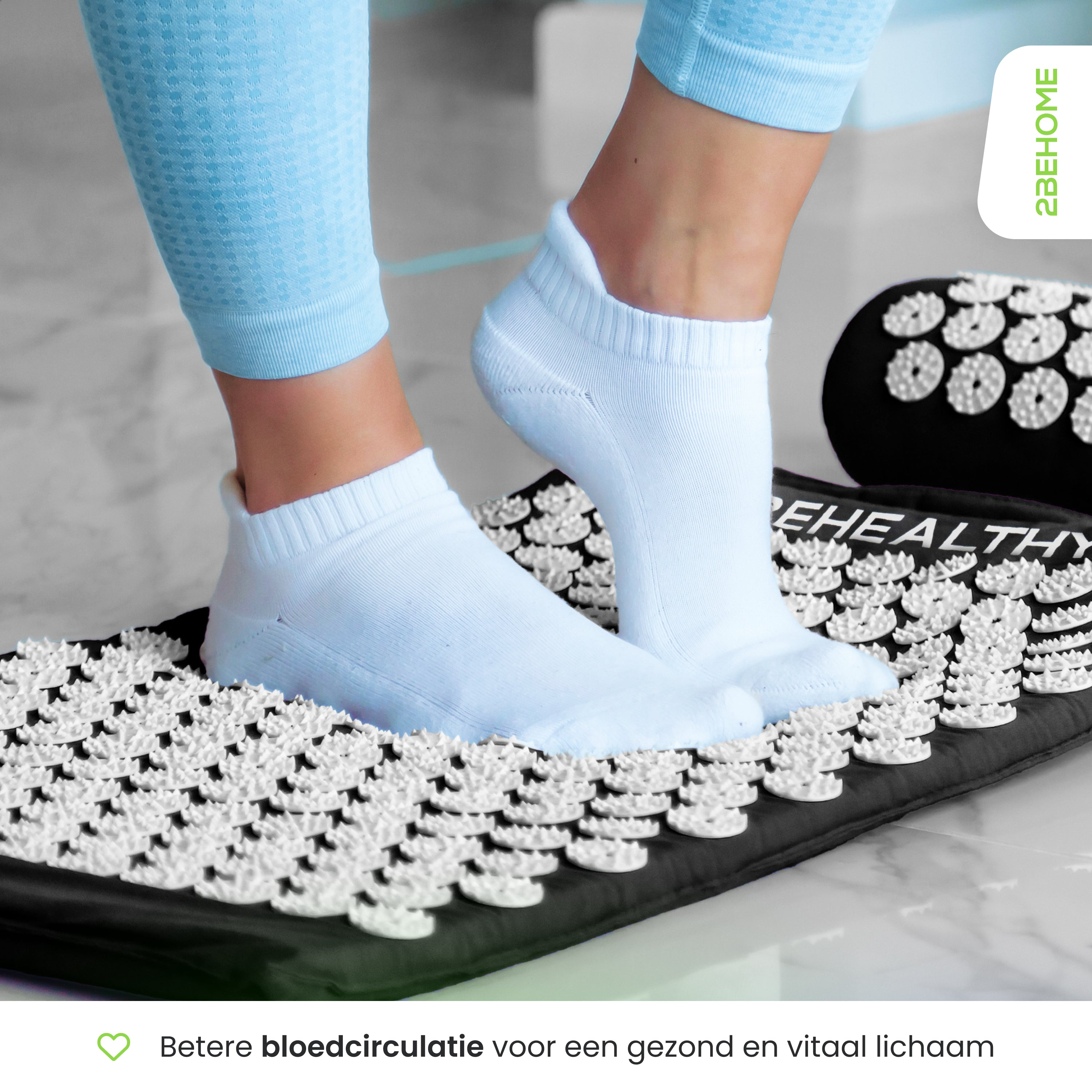 Feet wearing white socks on a black acupressure mat with white spikes.