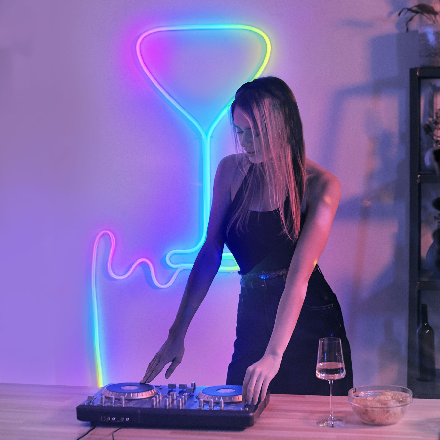 Donna DJ davanti a un bicchiere di vino al neon. Attrezzatura DJ e bicchiere sul tavolo.