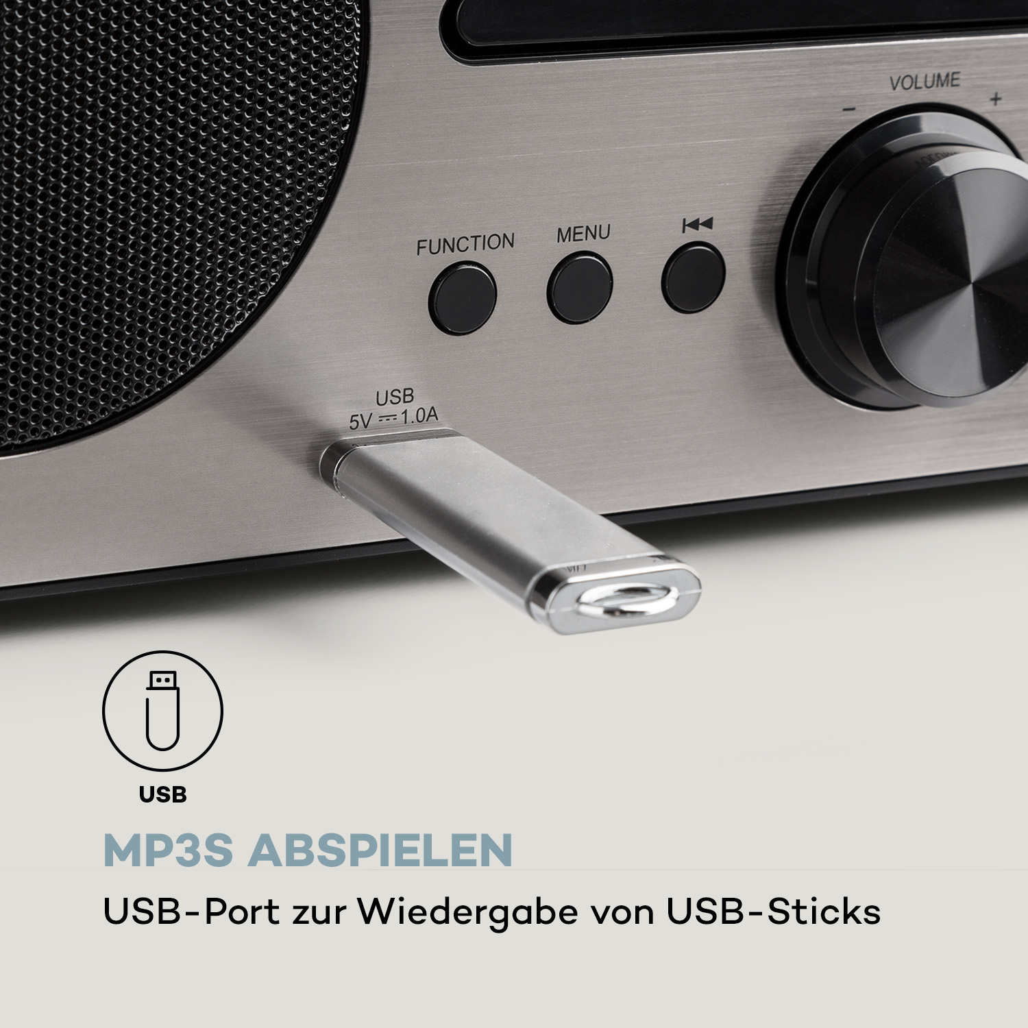 Ein USB-Stick, der in eine silberne Stereoanlage mit Lautstärke- und Funktionstasten gesteckt wird.