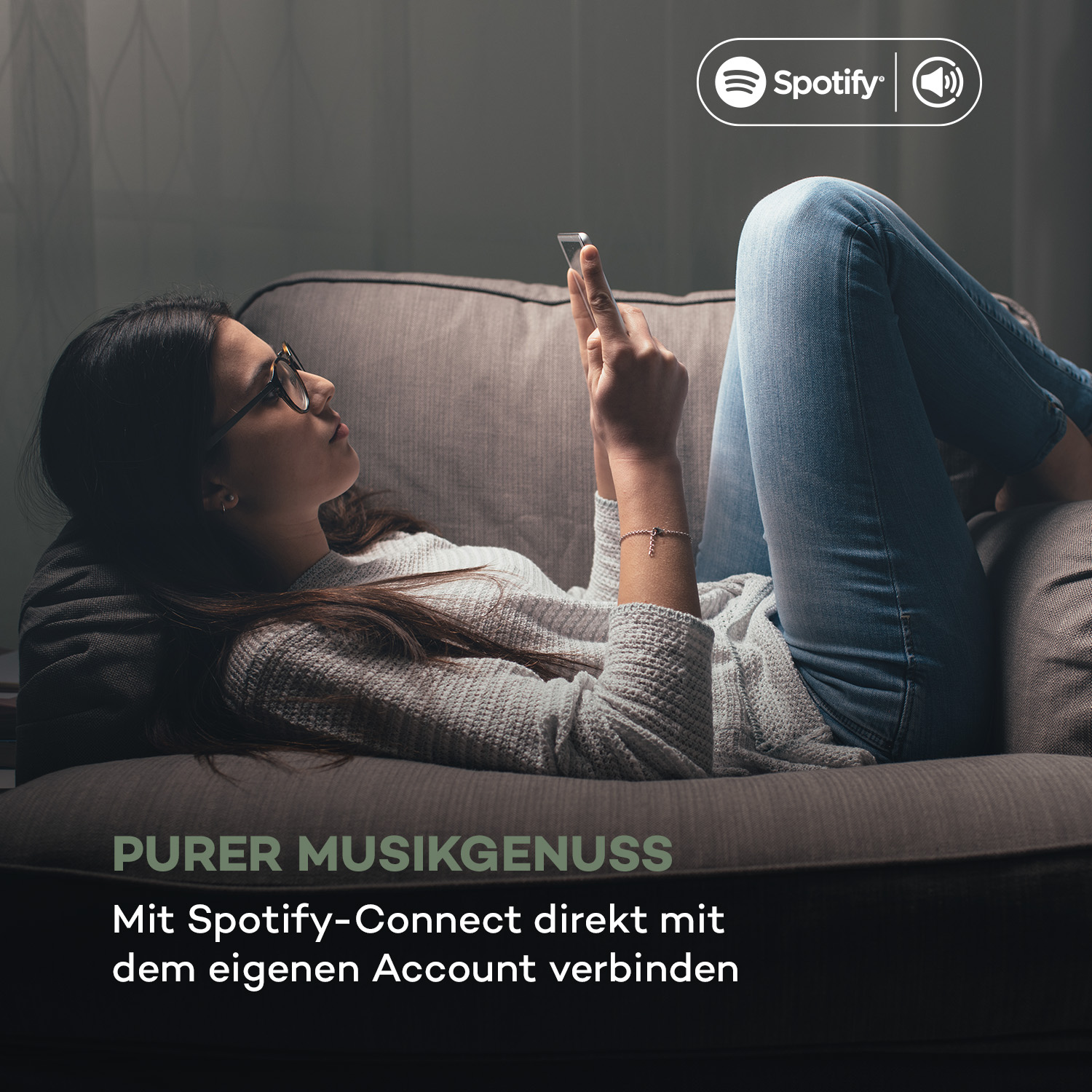 Eine Frau auf einer Couch benutzt ein Telefon mit dem Spotify-Logo. Text: Reiner Musikgenuss.