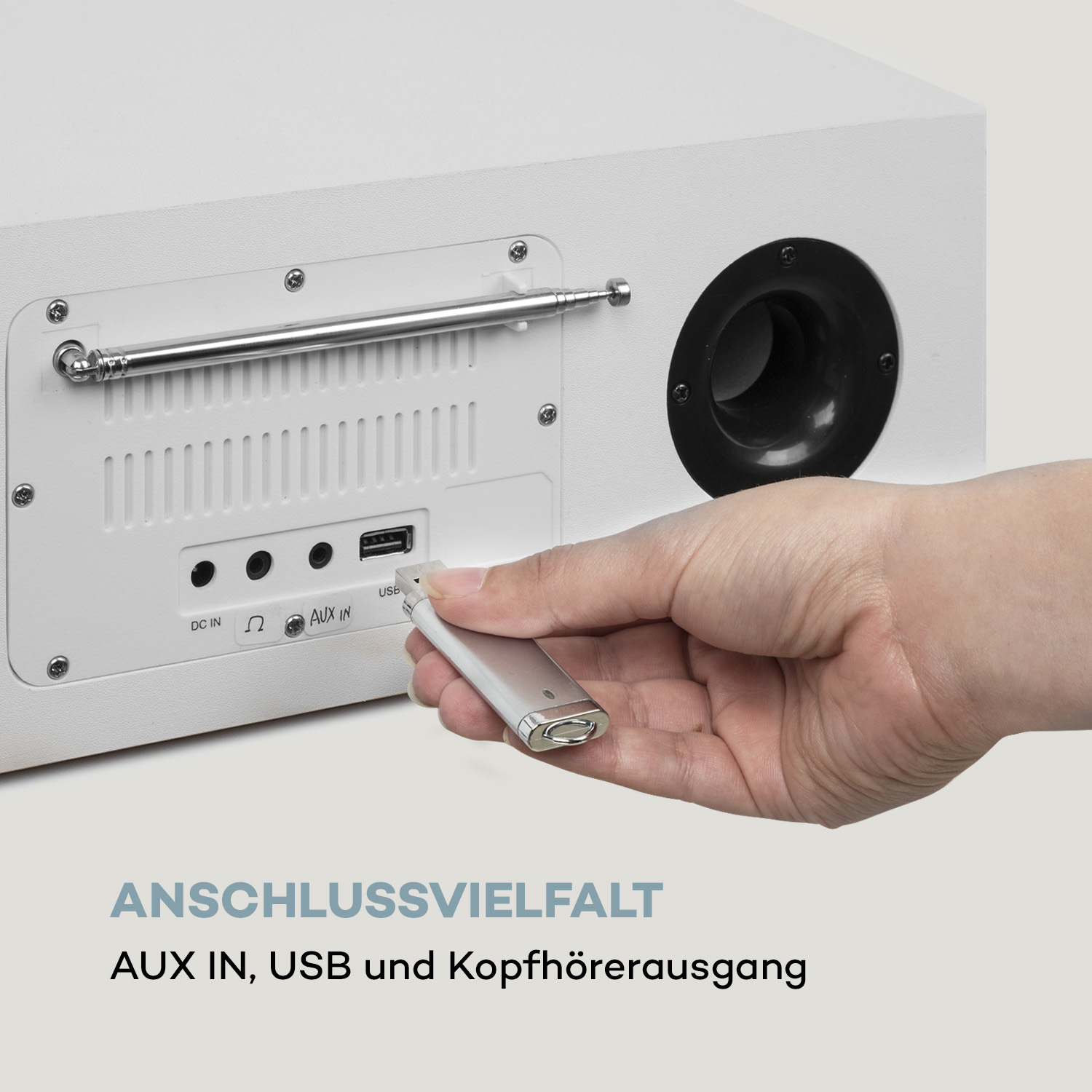 Eine Hand, die einen USB-Stick in die Rückseite einer weißen Stereoanlage einführt.