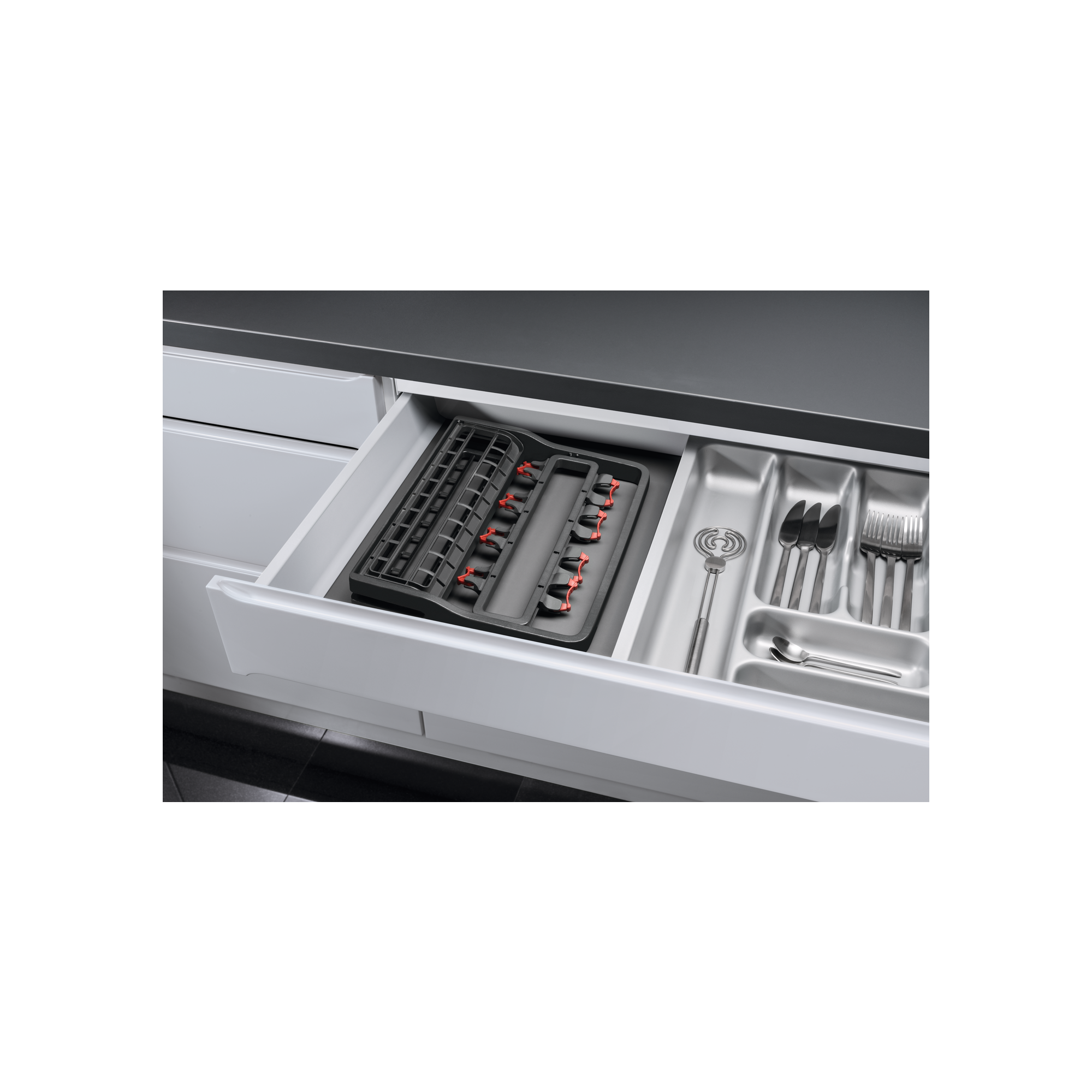 Otwarta szuflada z uporządkowanymi sztućcami i przyborami kuchennymi w kuchni.