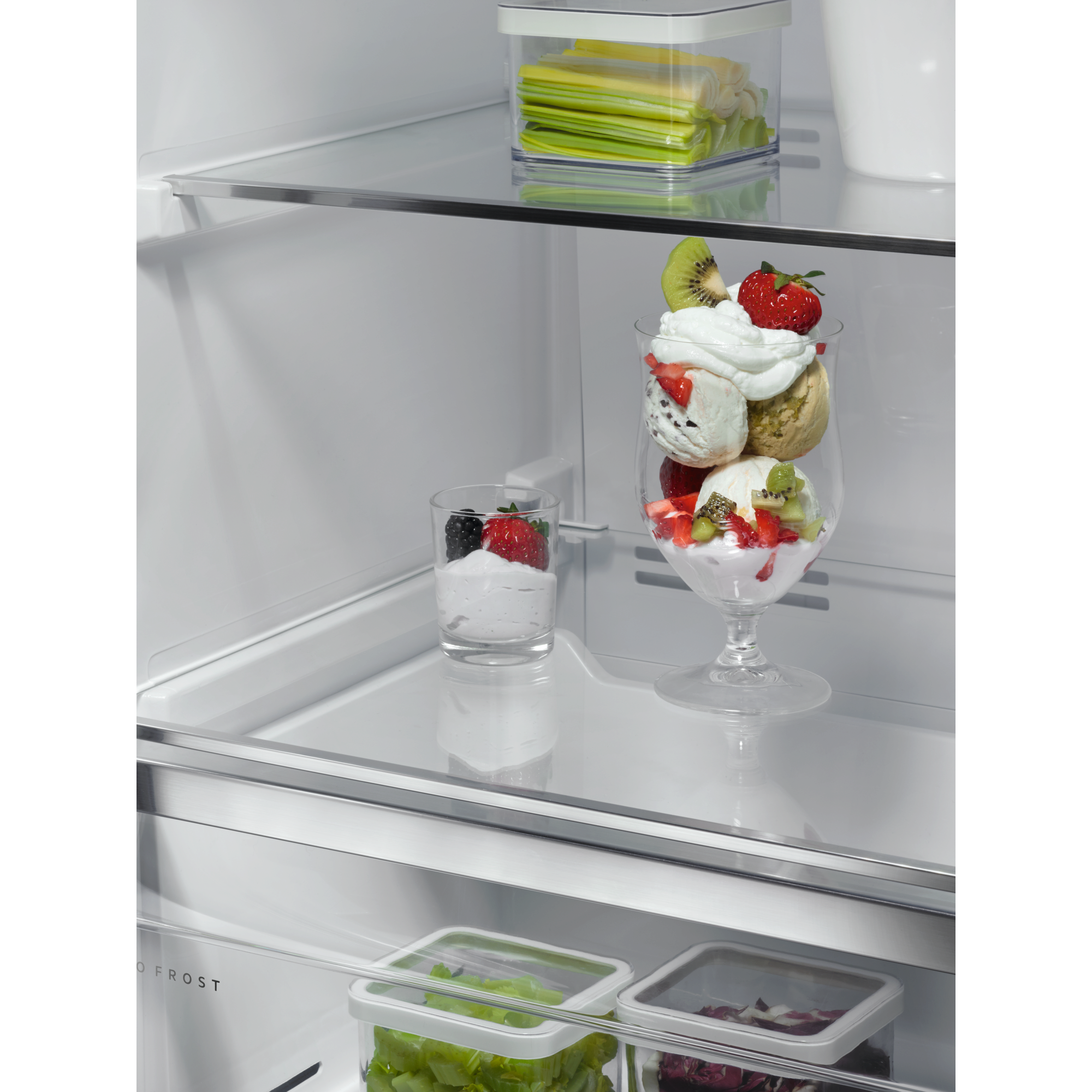 Interior de refrigerador. Estantes de vidrio. Copa de helado en vaso alto. Contenedores de fruta fresca.