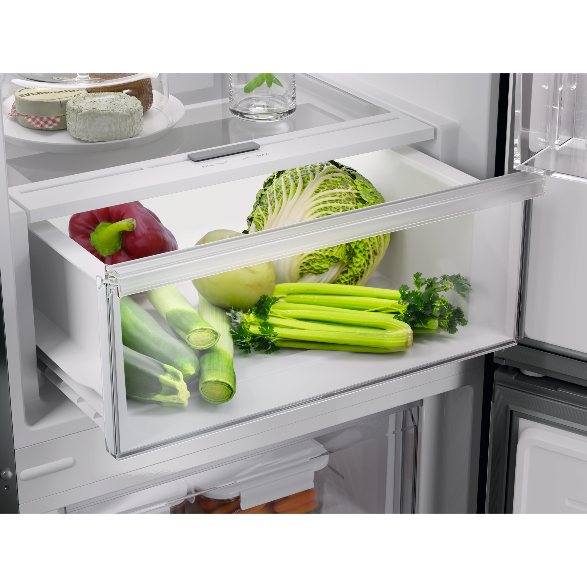 Cajón de refrigerador abierto. Contiene vegetales frescos: pimiento rojo, lechuga, puerros, apio y una manzana.