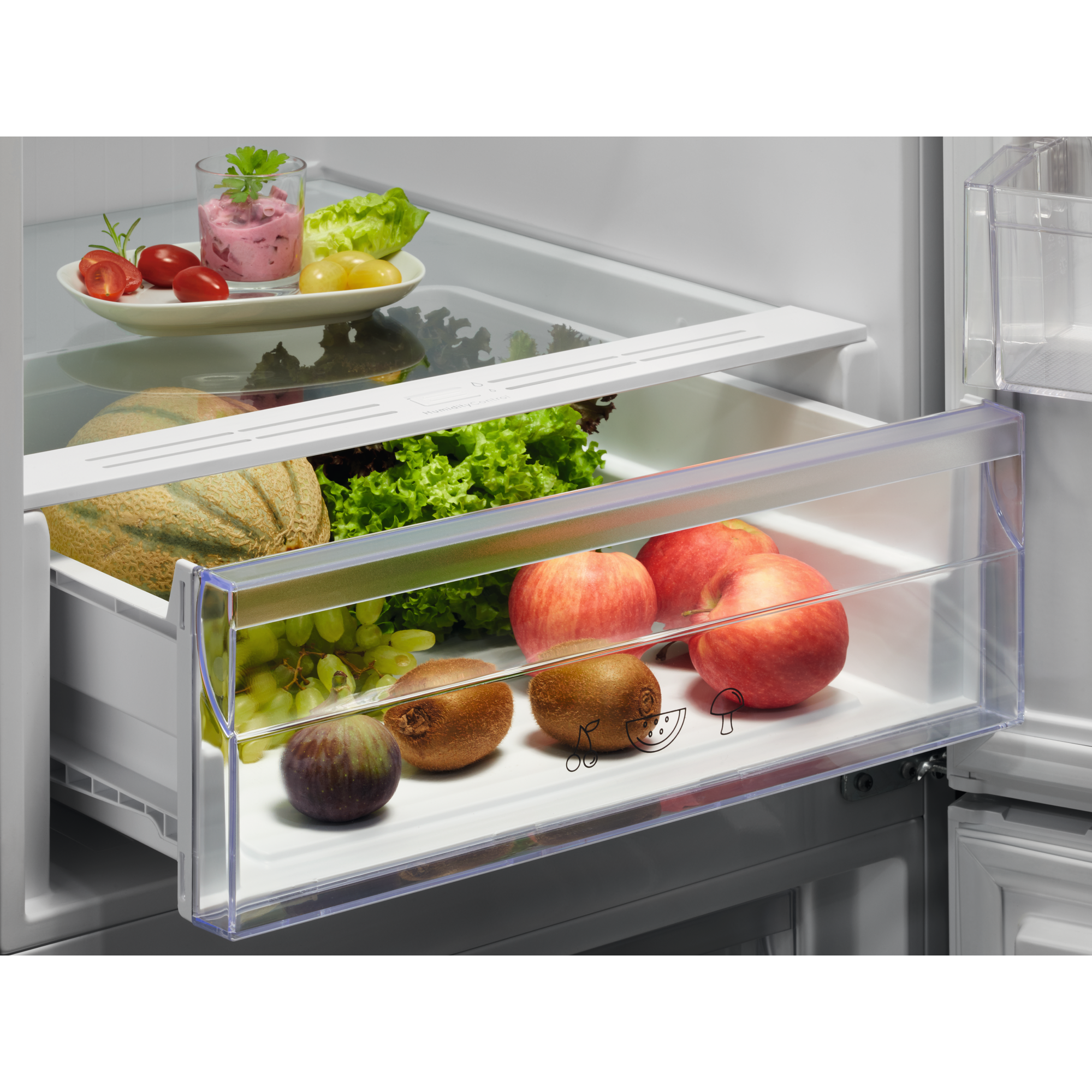 Kühlschrank mit Schublade voller Obst und Gemüse. Glasablage darüber.
