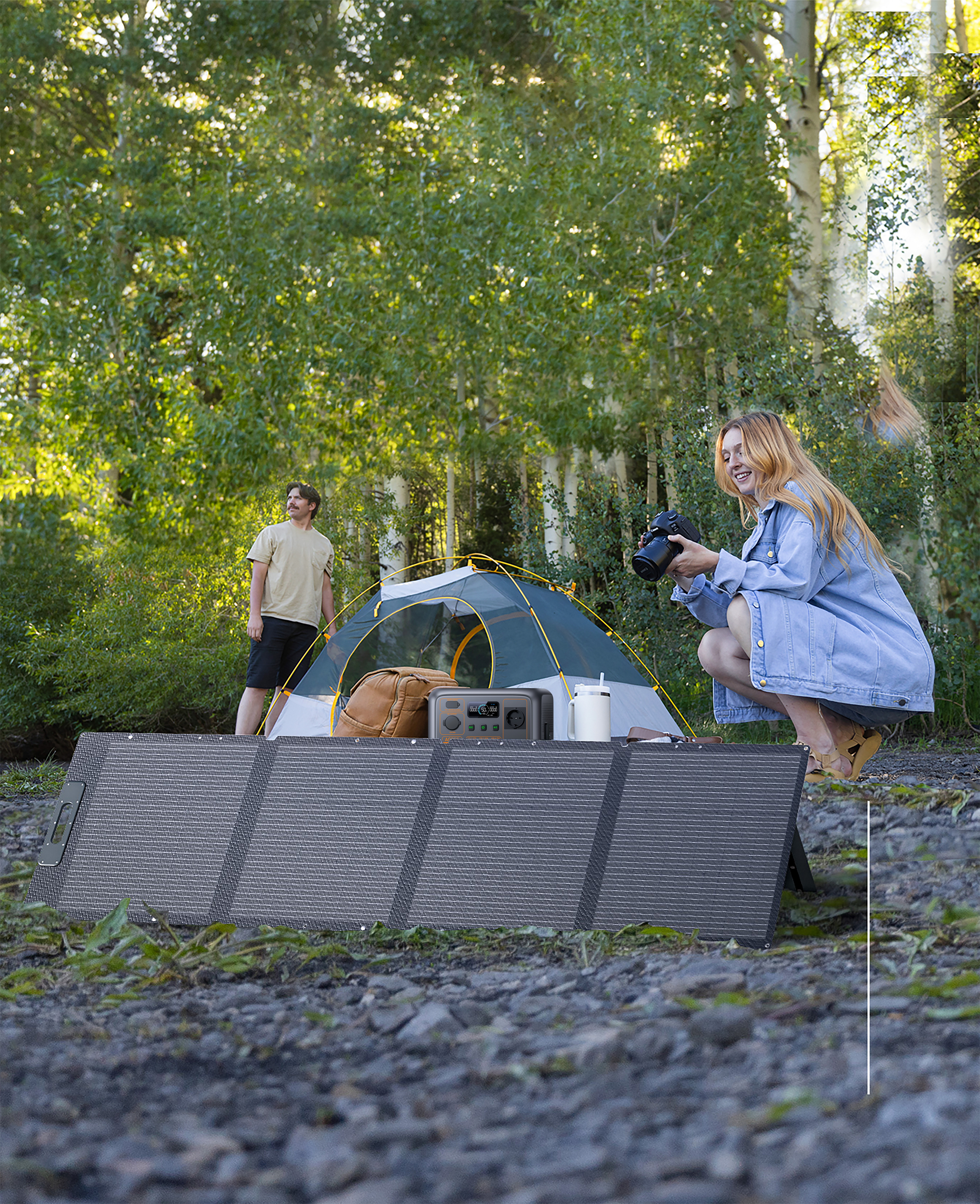 Kobieta robi zdjęcie namiotu, za nią stoi mężczyzna, w otoczeniu lasu.