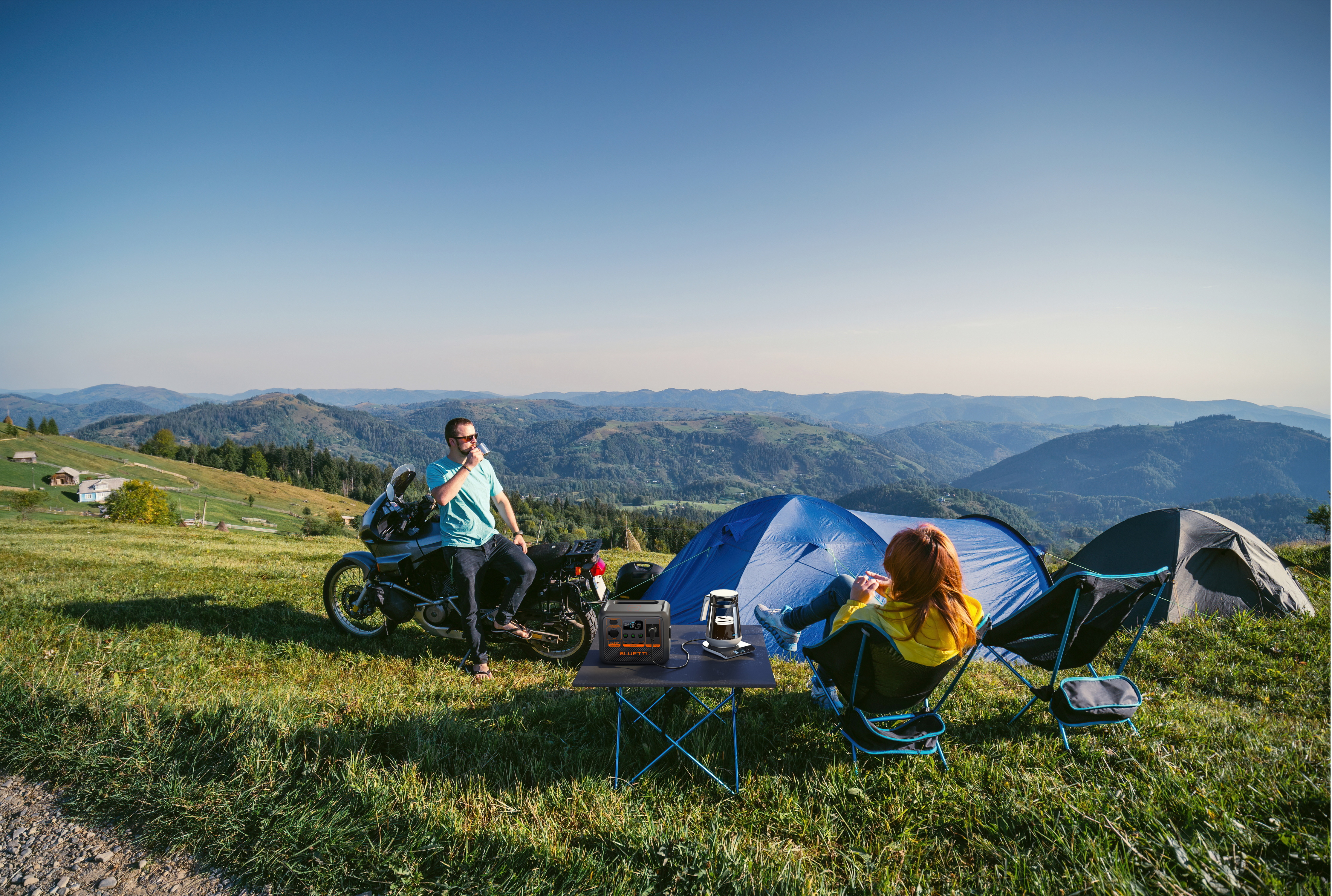 Para kempingująca w pobliżu gór, obok motocykla, z przenośną stacją zasilania.