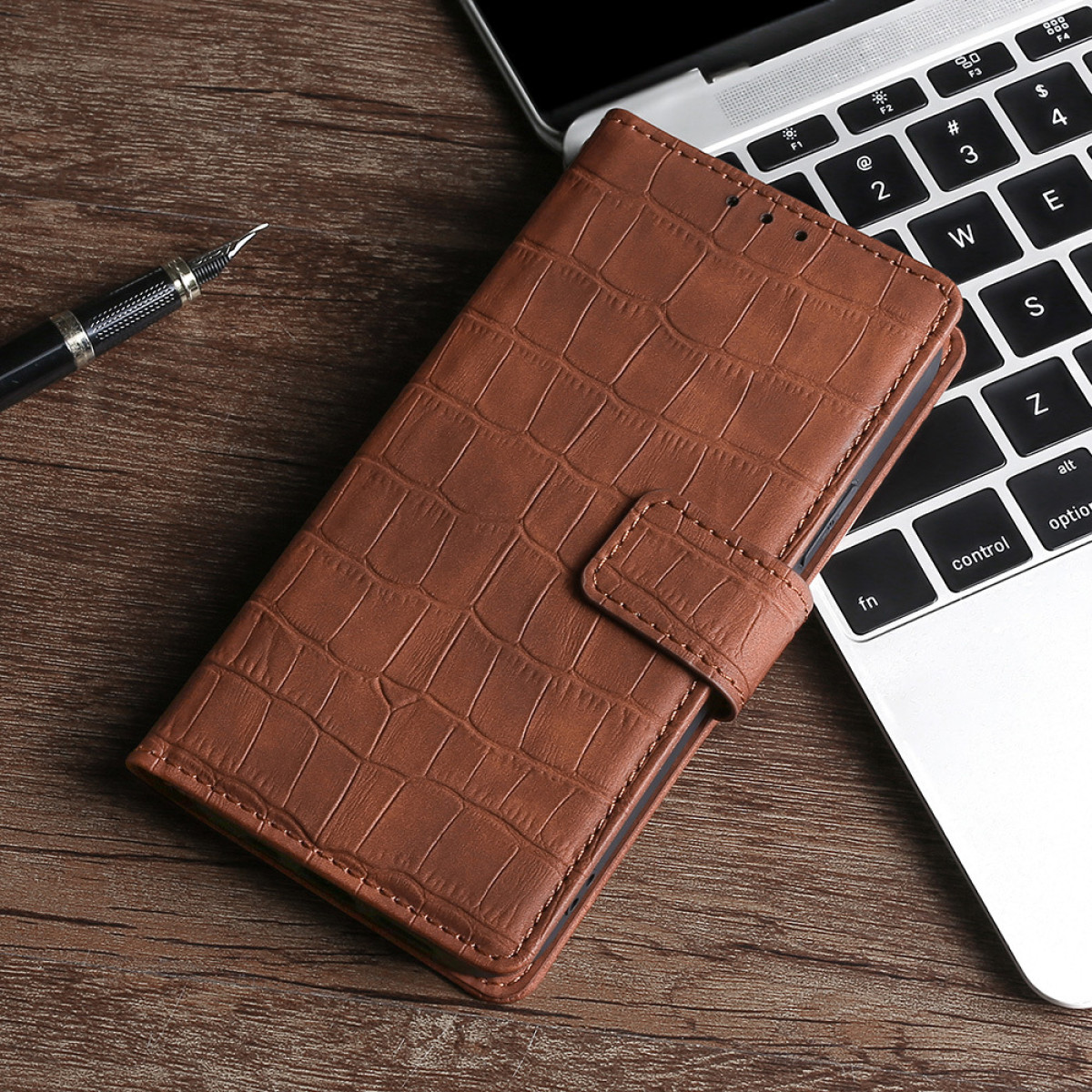 Custodia per telefono in pelle marrone su una scrivania di legno vicino a un laptop e una penna.