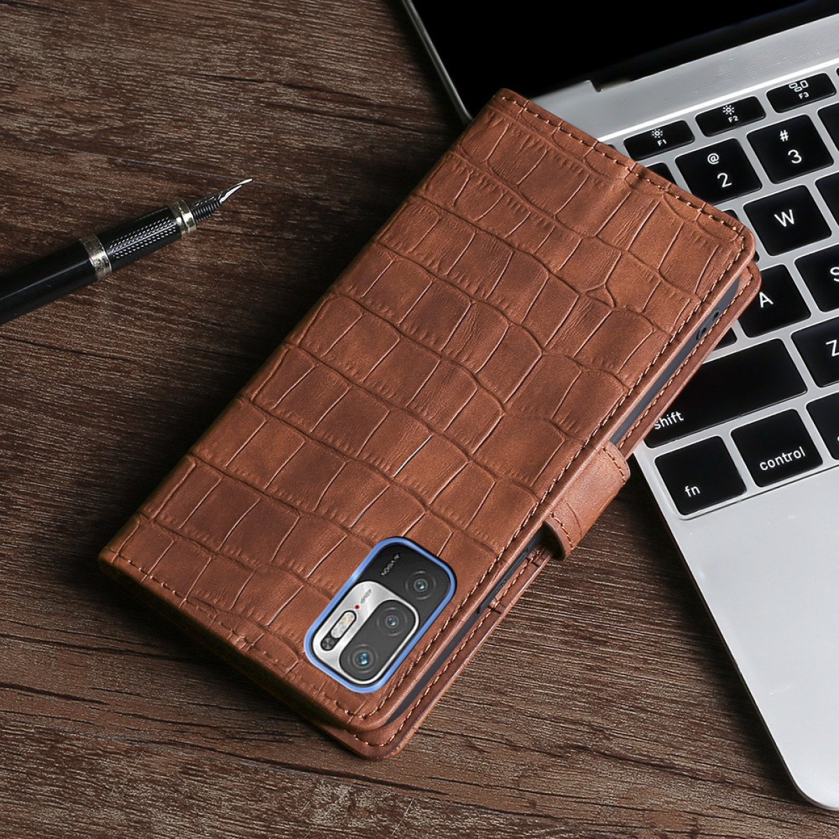 Custodia per telefono in pelle marrone su un tavolo di legno accanto a un laptop e una penna.