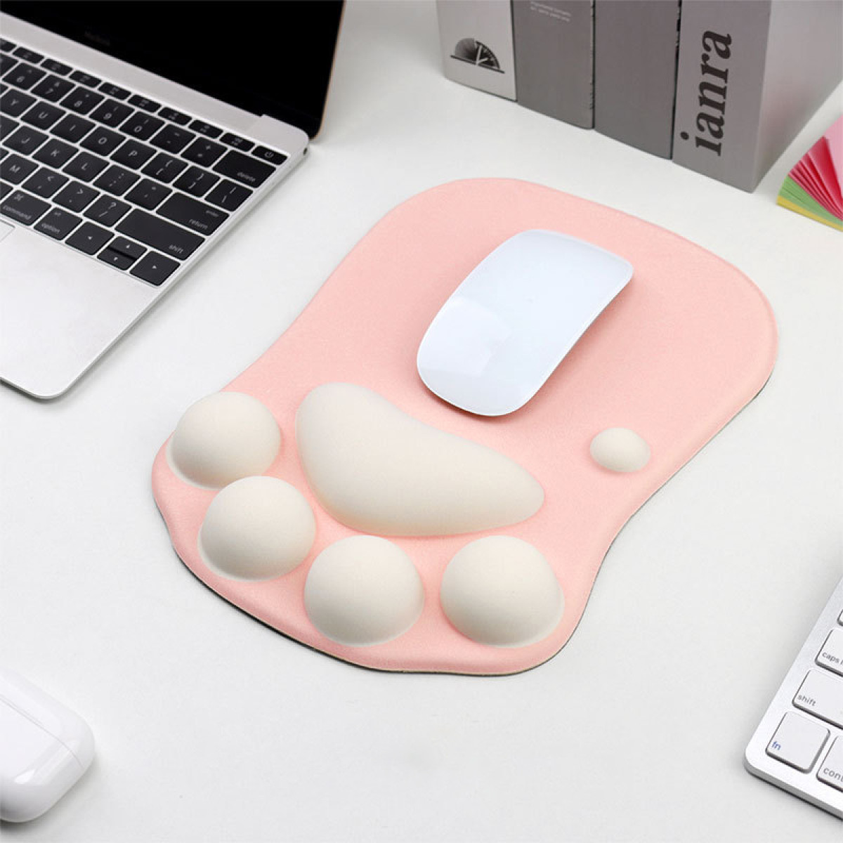Ein pinkfarbenes, pfotenartiges Mauspads mit einer weißen Maus. Ein Laptop ist oben links.