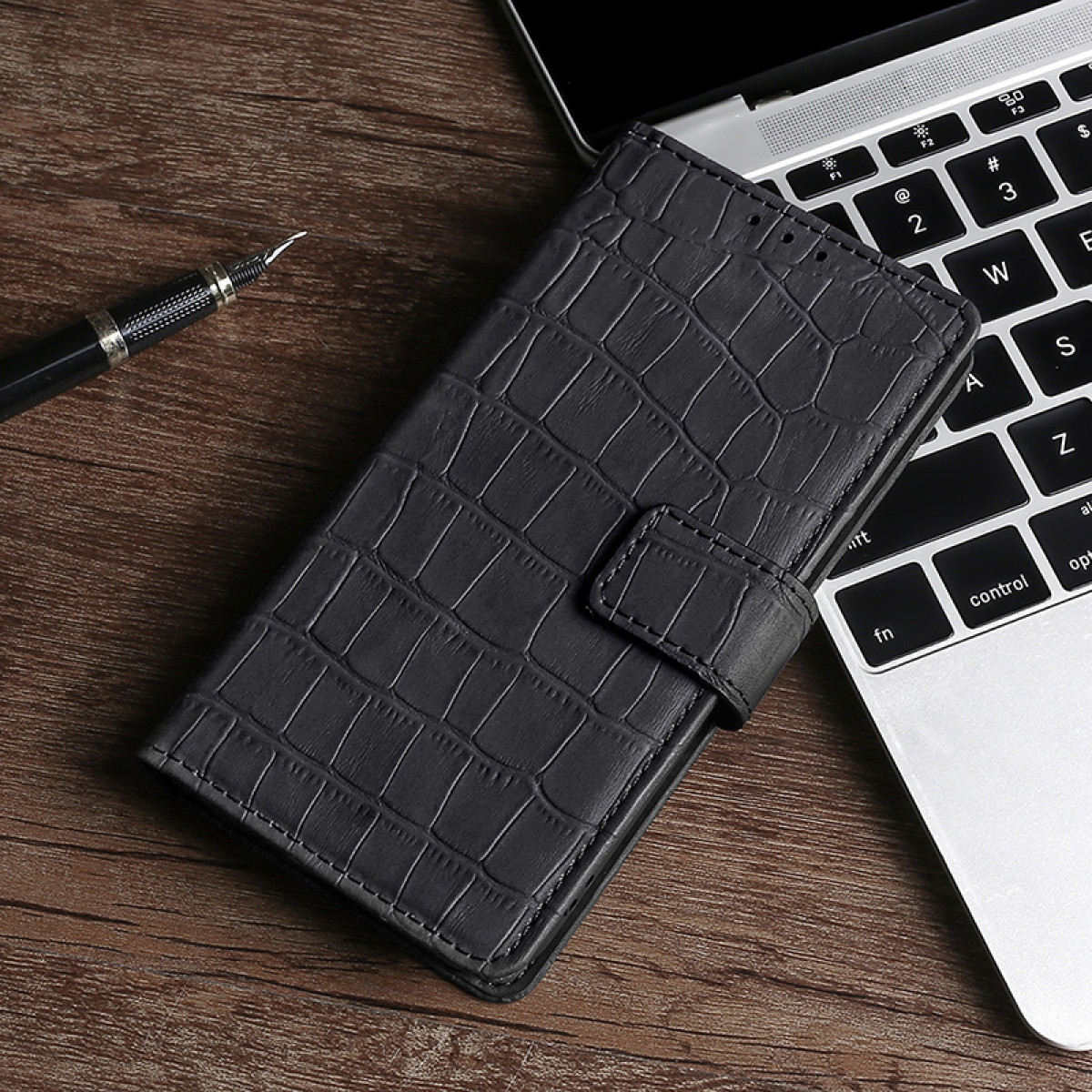 Una custodia per telefono nera con motivo a coccodrillo su un laptop. Accanto c'è una penna.