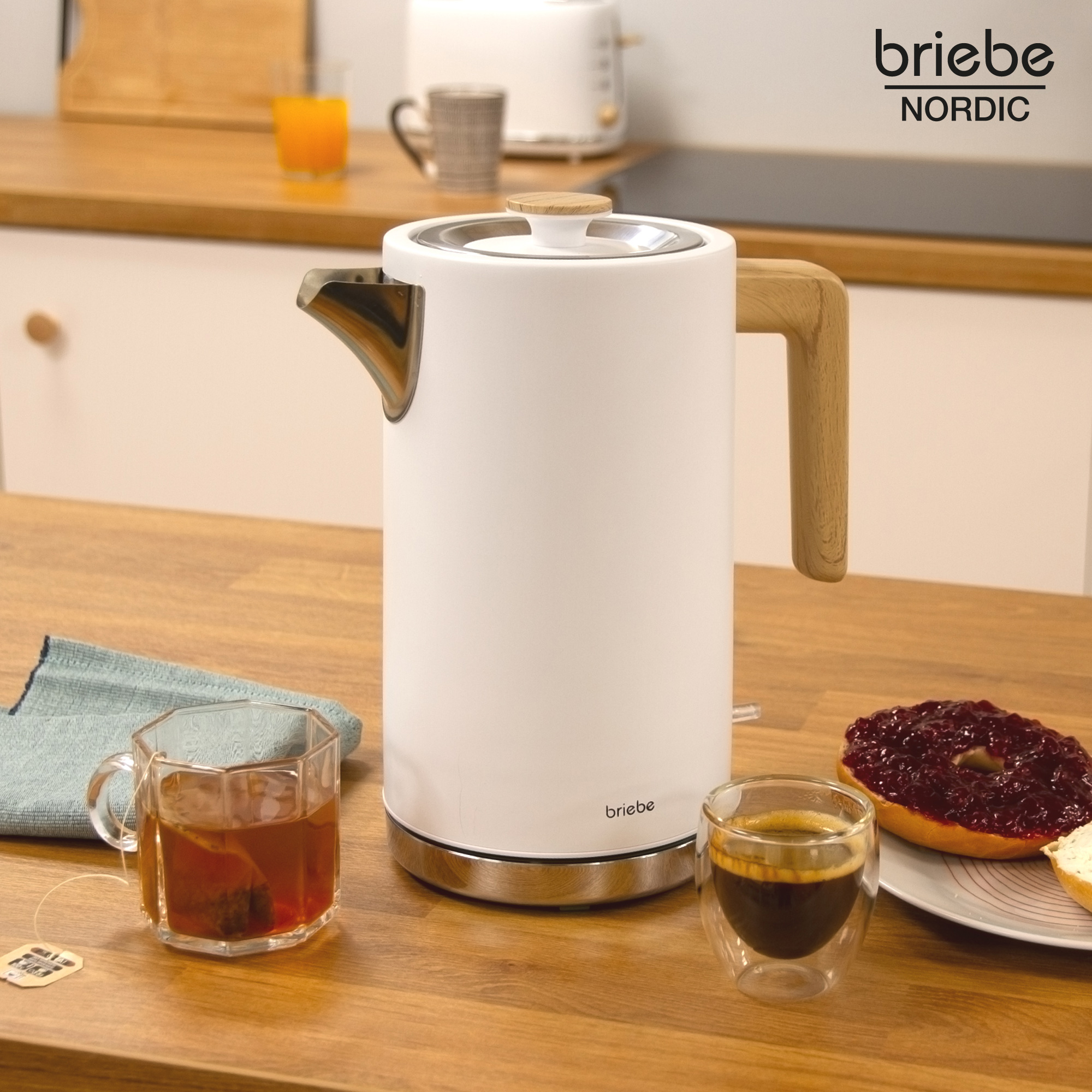 Una tetera eléctrica blanca con asa de madera y una taza de té junto a una tostada con mermelada.
