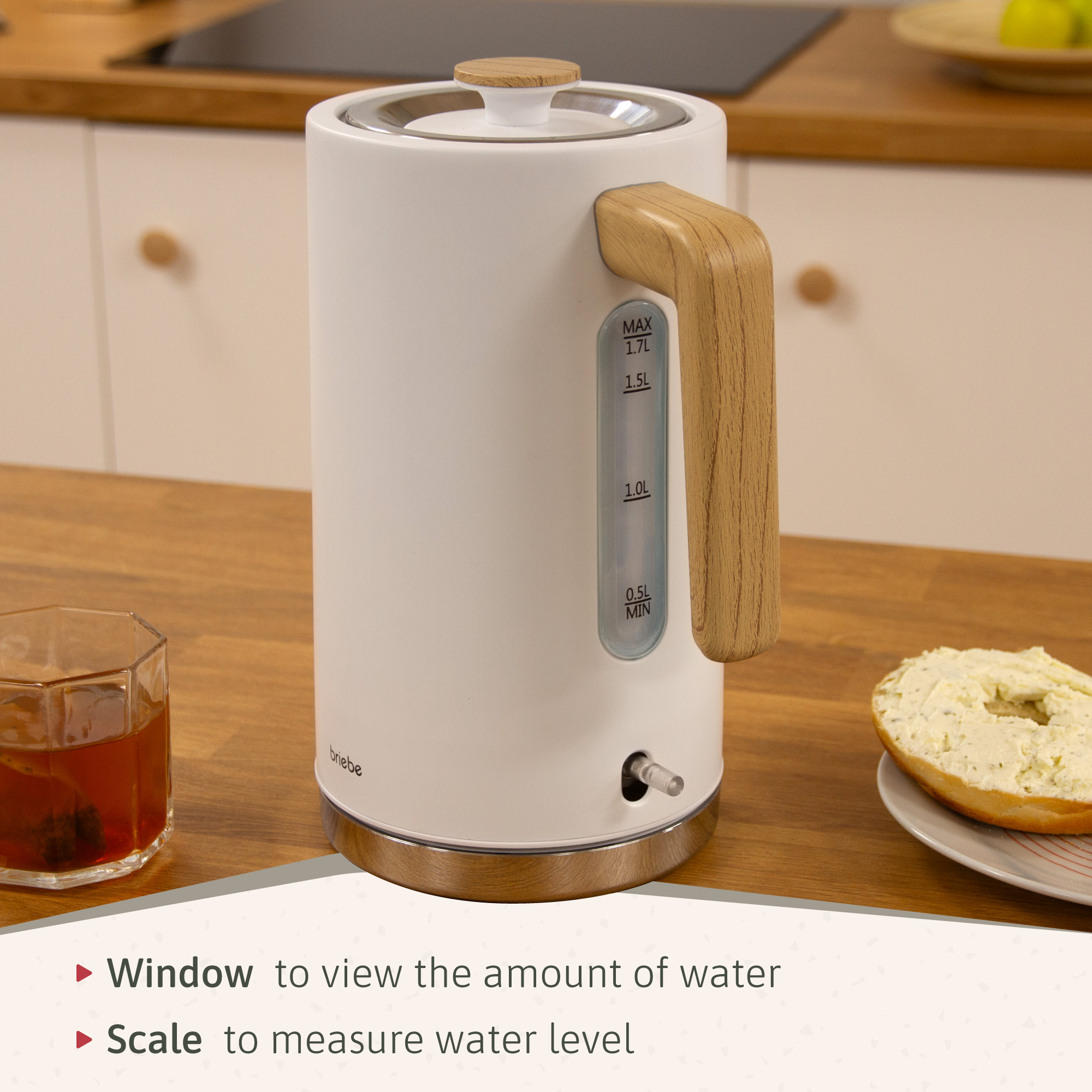 Hervidor eléctrico blanco con asa de madera, ventana de nivel de agua y marcas. Un bagel está en un plato.