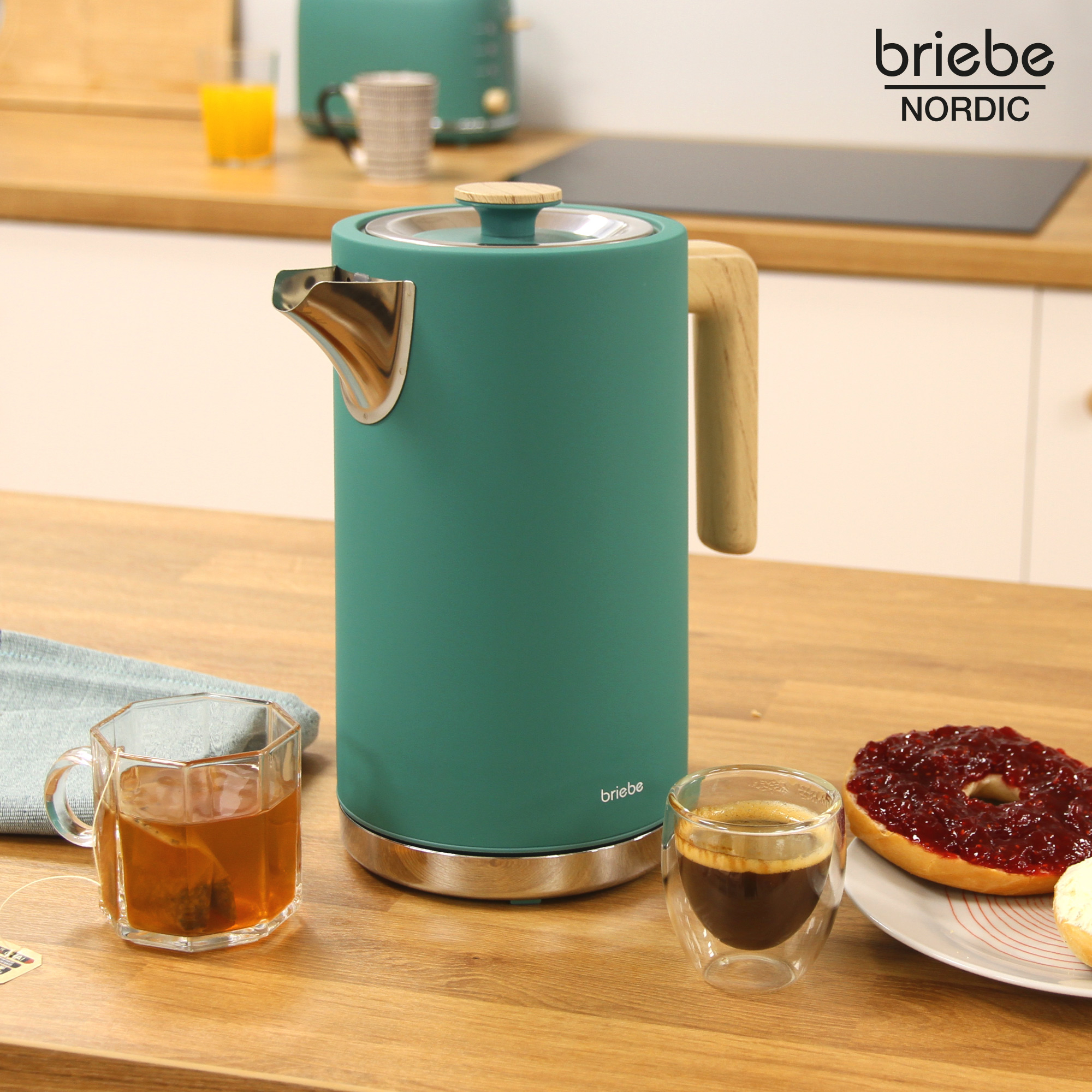 Una tetera turquesa con asa de madera y boquilla plateada sobre una mesa de madera, con desayuno.