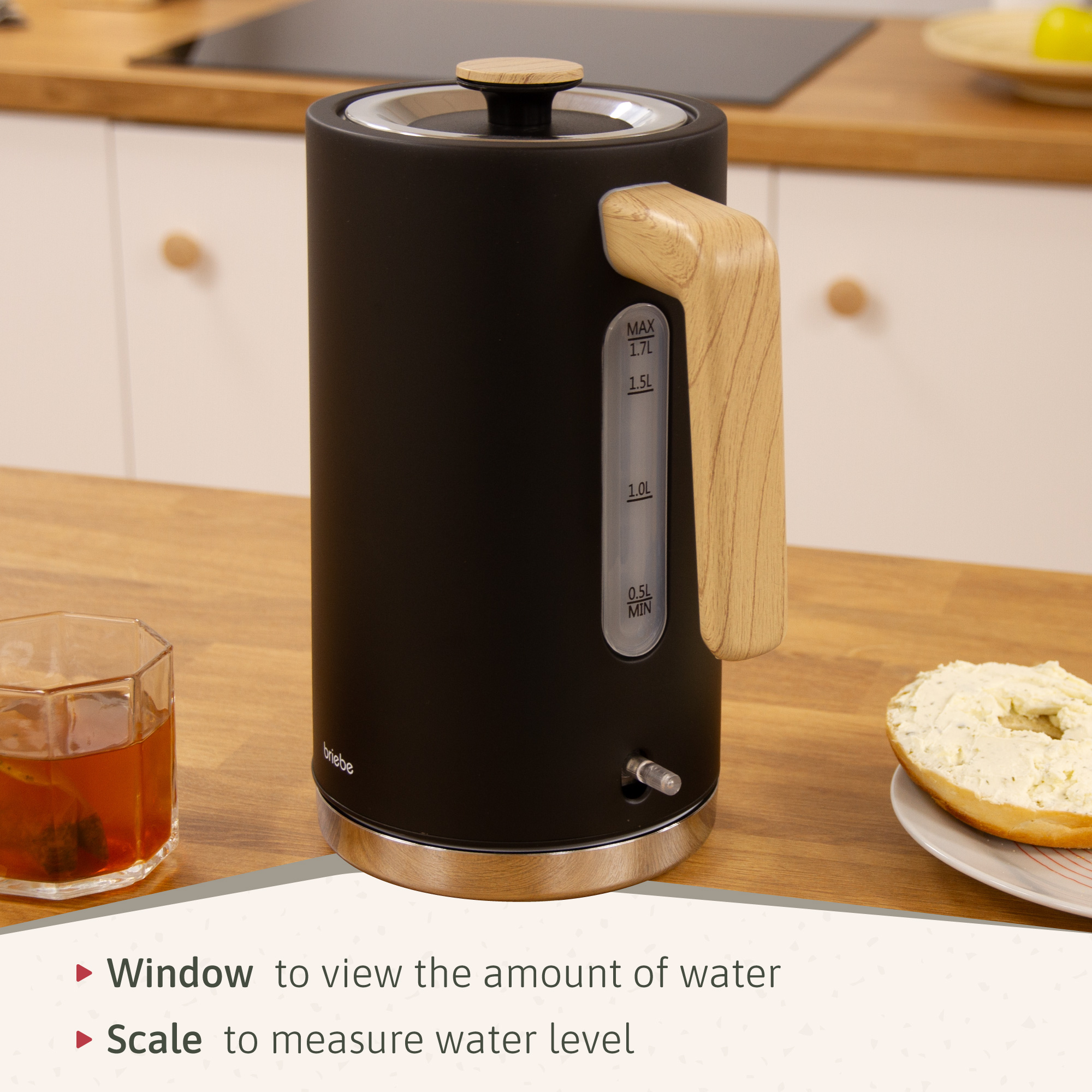 Hervidor eléctrico negro con mango de madera, junto a un vaso y un bagel.