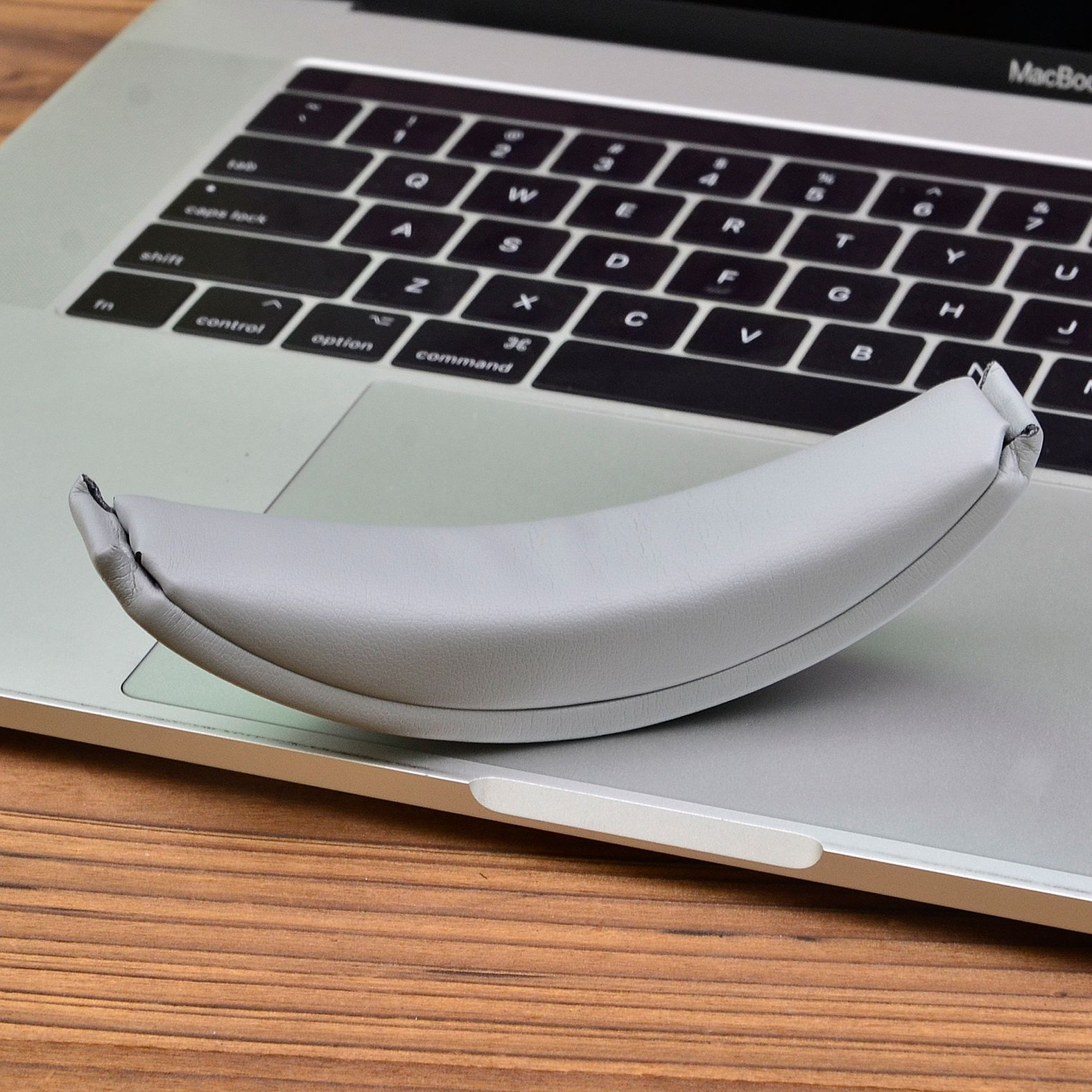 Un laptop grigio con un supporto imbottito grigio sopra la tastiera. Il supporto è curvo.
