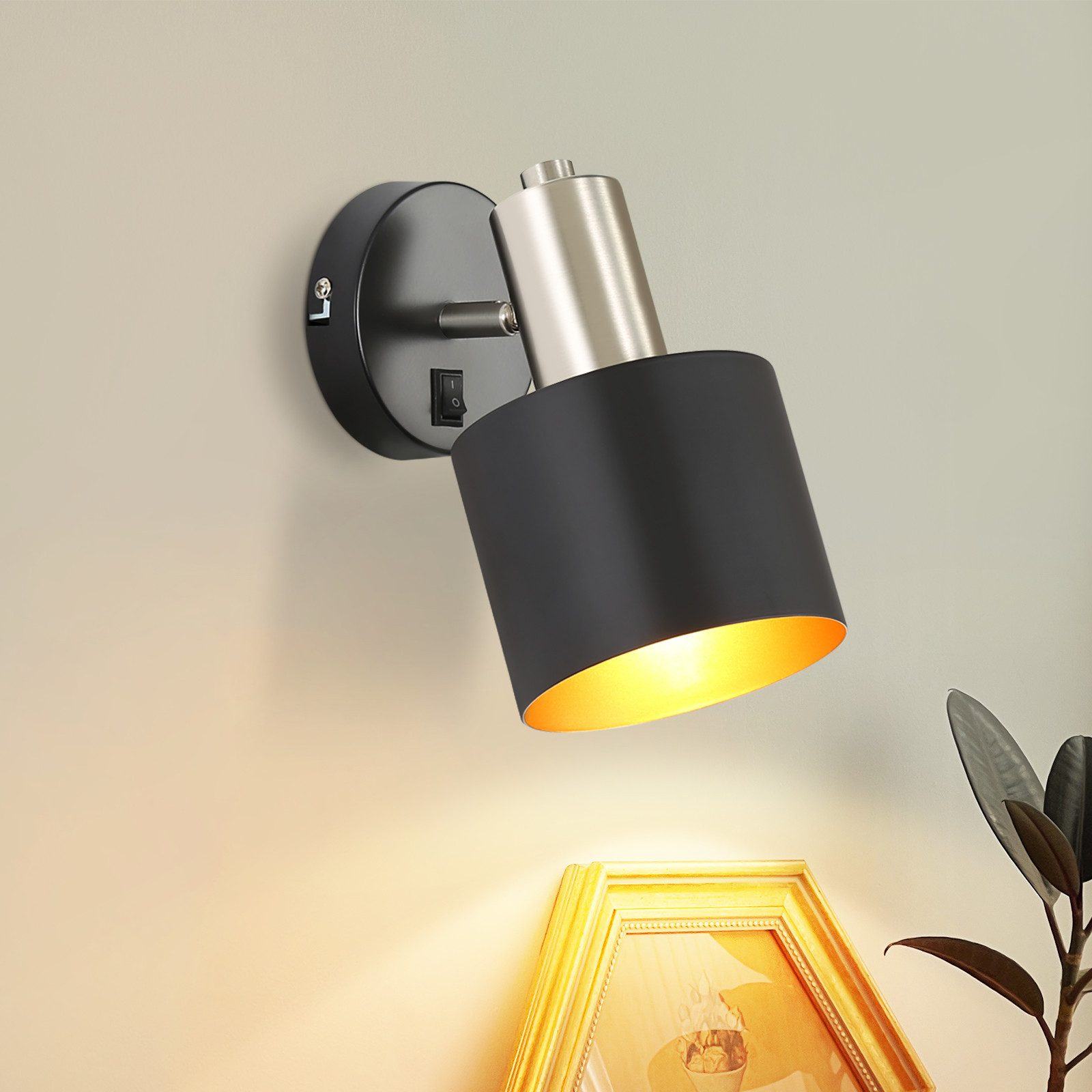 Una lampada da parete nera e argento montata su un muro beige. La lampada è rivolta verso il basso.