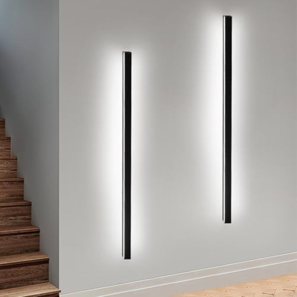 Due luci a LED nere illuminano una parete bianca. Scale in legno visibili a sinistra.