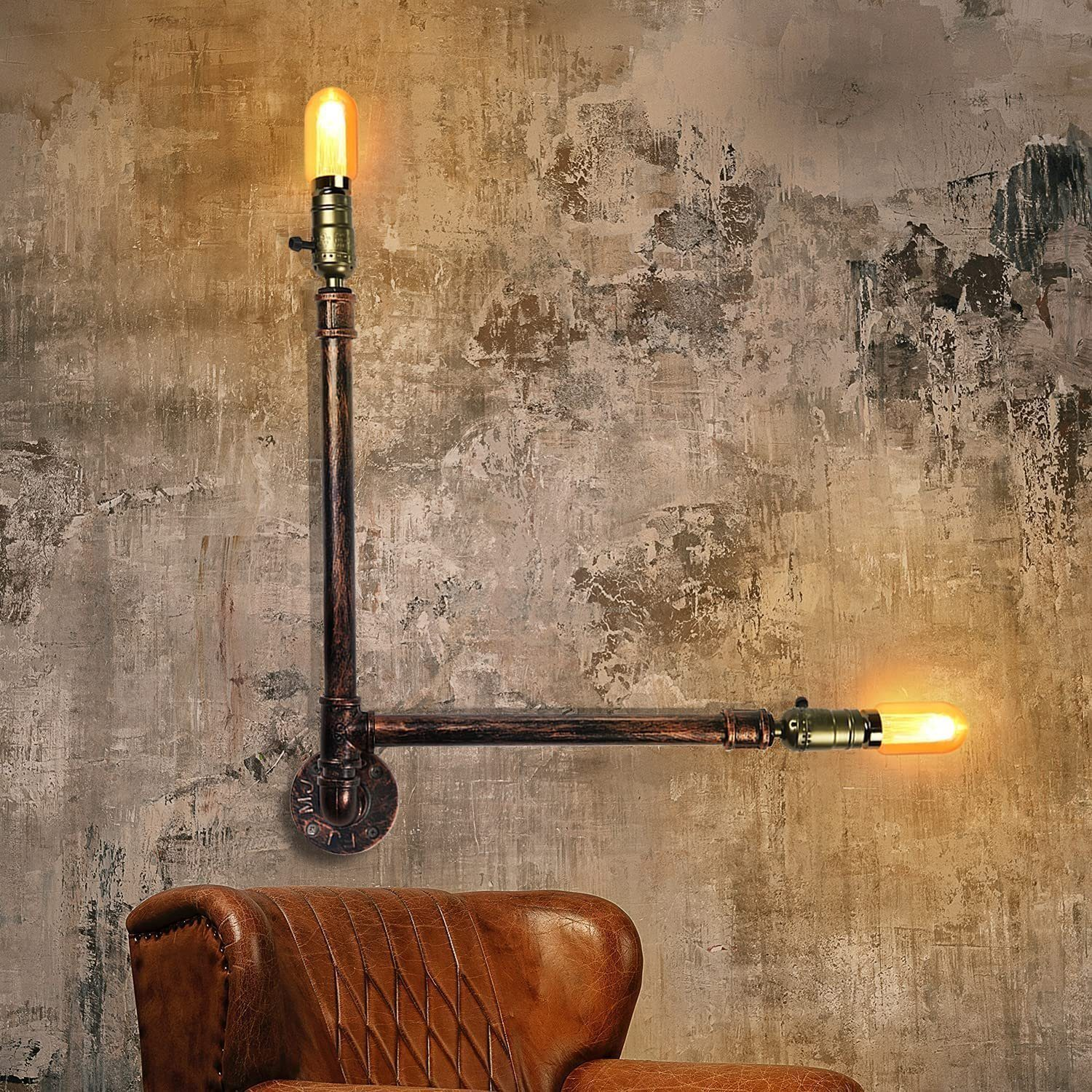 Lampada da parete in stile industriale con due lampadine a vista, montata su un muro strutturato, sopra una poltrona in pelle.