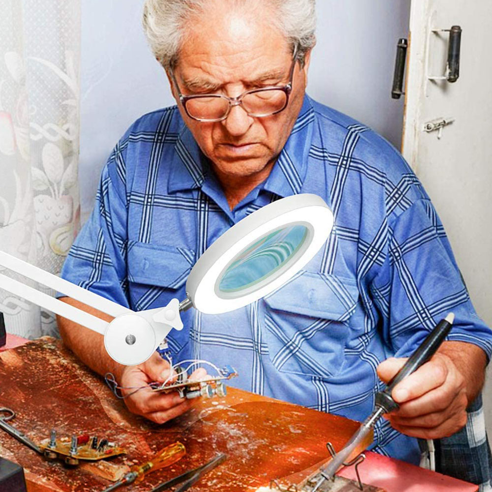 Ein älterer Mann mit Brille benutzt eine beleuchtete Lupe, um eine Leiterplatte zu untersuchen.
