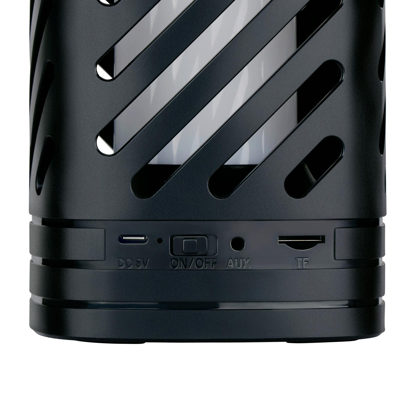 Zwarte speaker met metalen rooster, knoppen en poorten. Wit licht binnenin. Zwarte achtergrond.