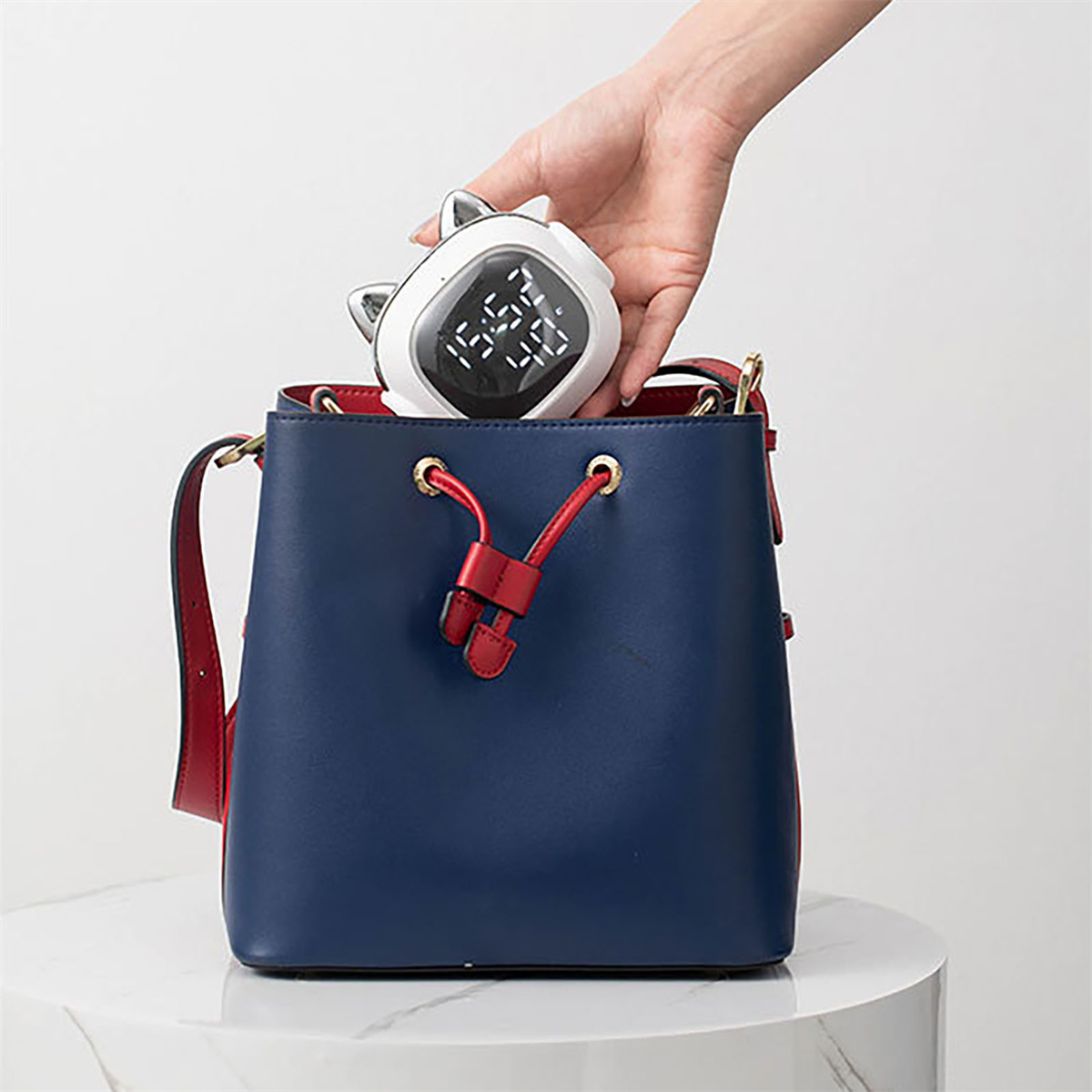 Hand, die einen weißen katzenförmigen Wecker in eine blaue Handtasche legt.
