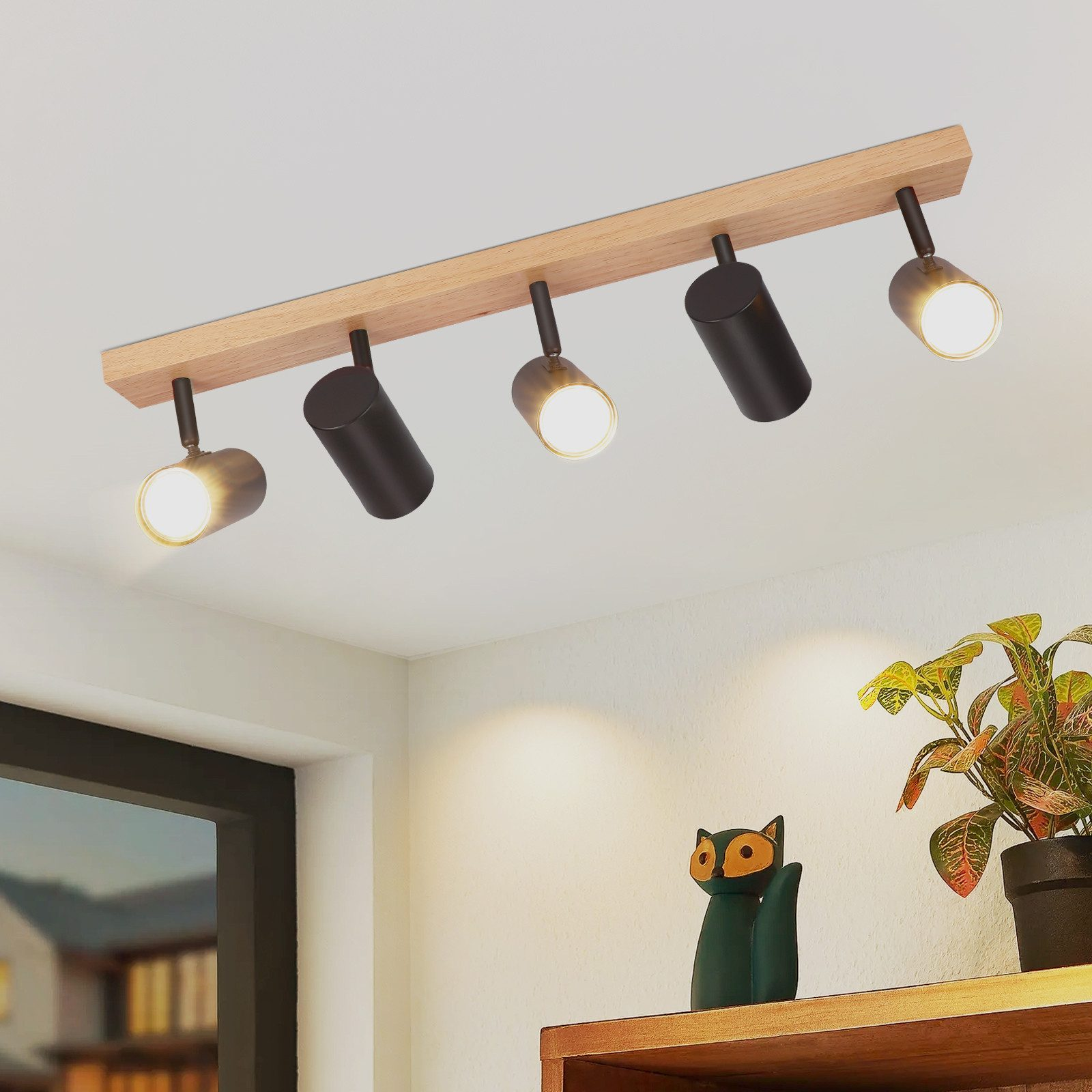 Illuminazione a binario montata a soffitto con cinque faretti neri su una trave di legno e un arredo.