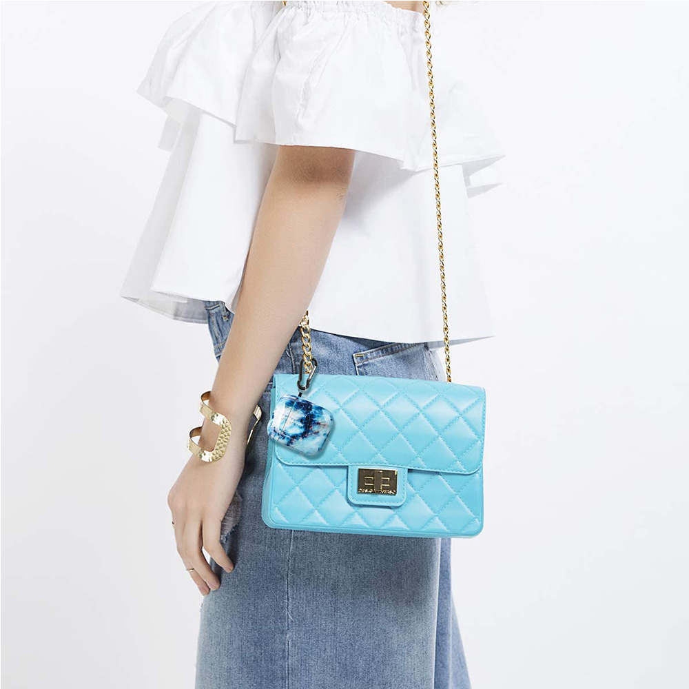 Eine Frau in weißem Hemd und Jeans, hält eine blaue gesteppte Handtasche mit goldener Kette.