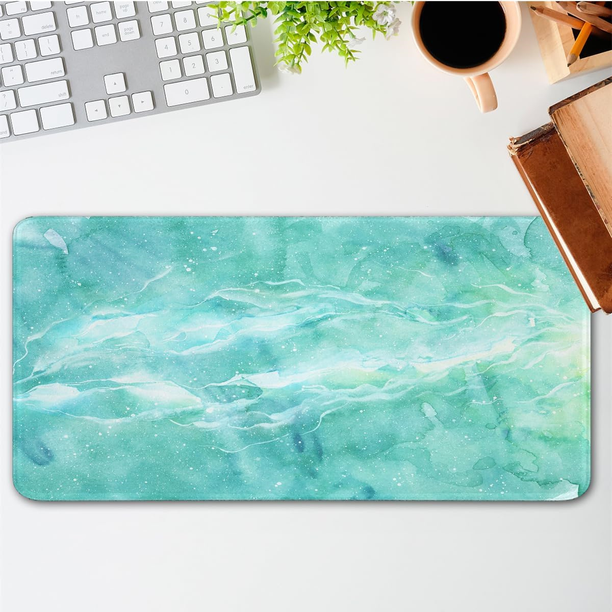 Eine Schreibtischunterlage mit Aquarelldesign in Türkis- und Weißtönen, mit Tastatur und Tasse.
