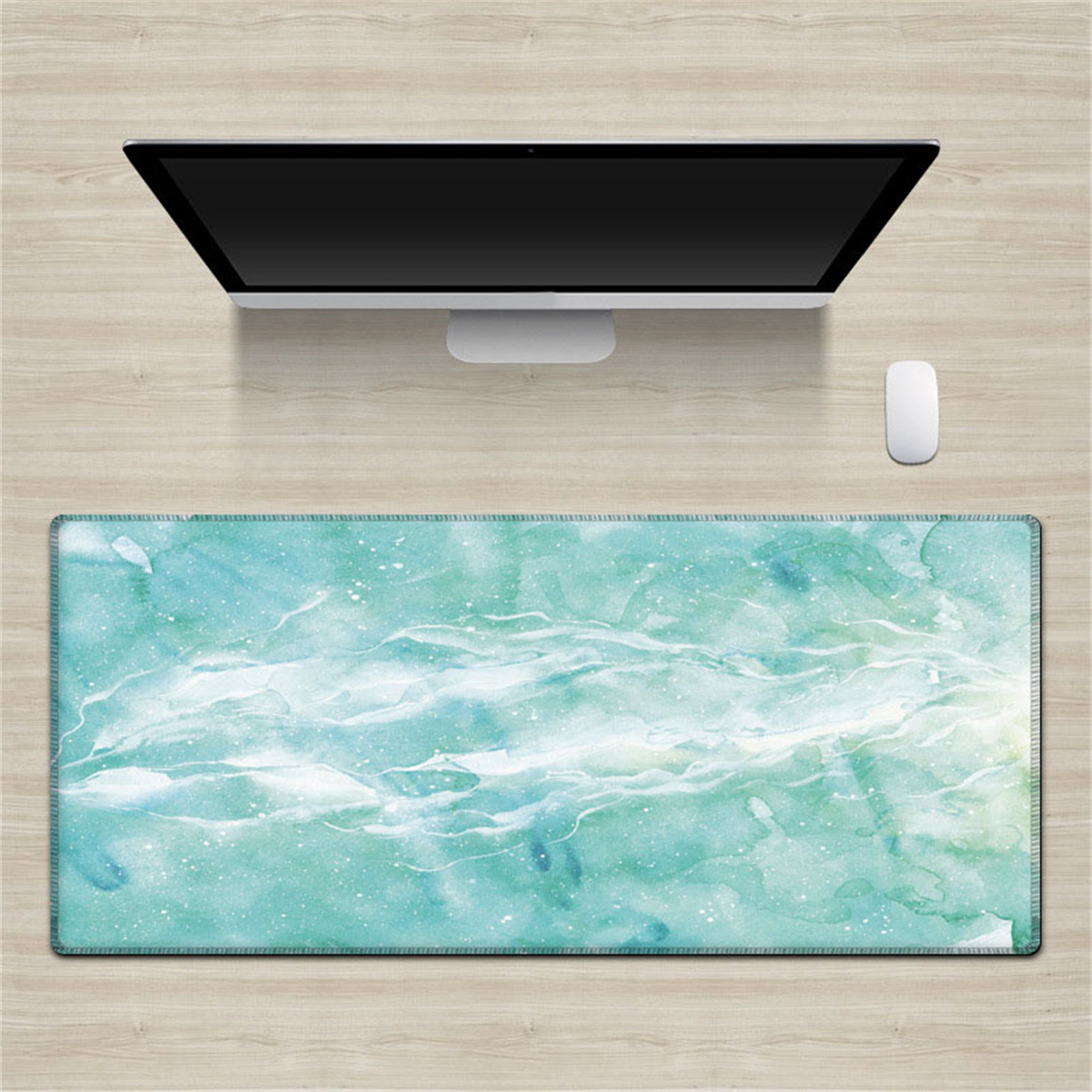 Schreibtisch-Setup: Monitor, Maus und eine türkisfarbene Schreibtischunterlage mit Aquarell-Design.