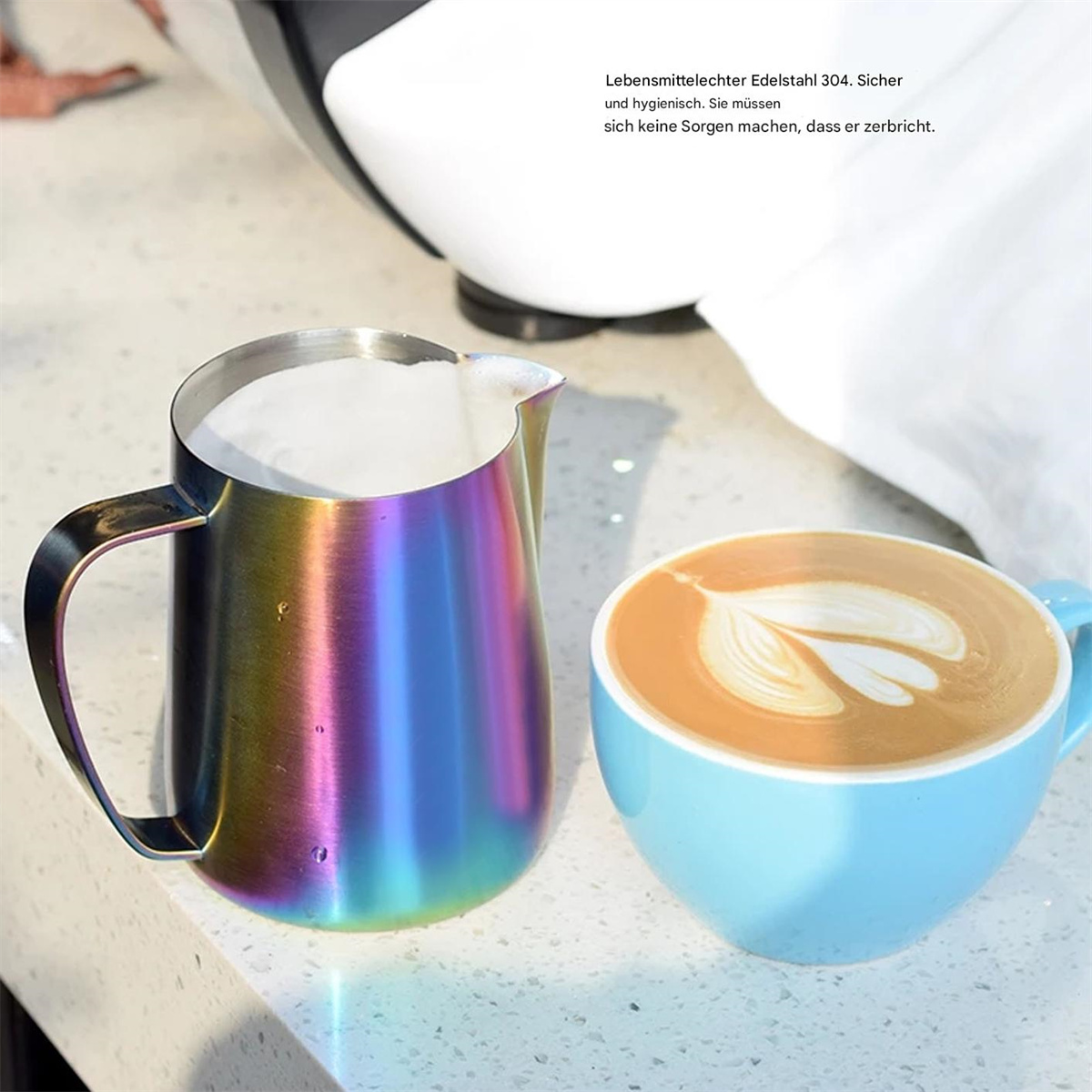 Ein regenbogenfarbener Krug und eine hellblaue Tasse mit Latte Art auf weißer Oberfläche.